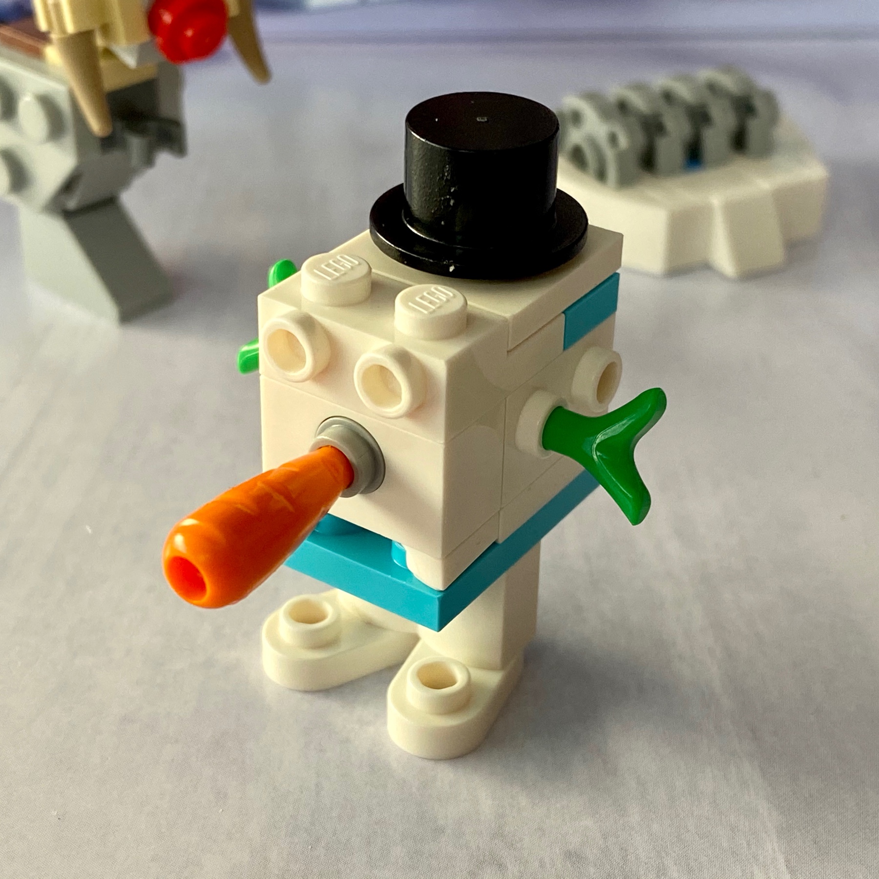 LEGO micro-build of a white Star Wars GONK droid dressed as a snowman with green sprout arms, orange carrot nose, and a black top hat.