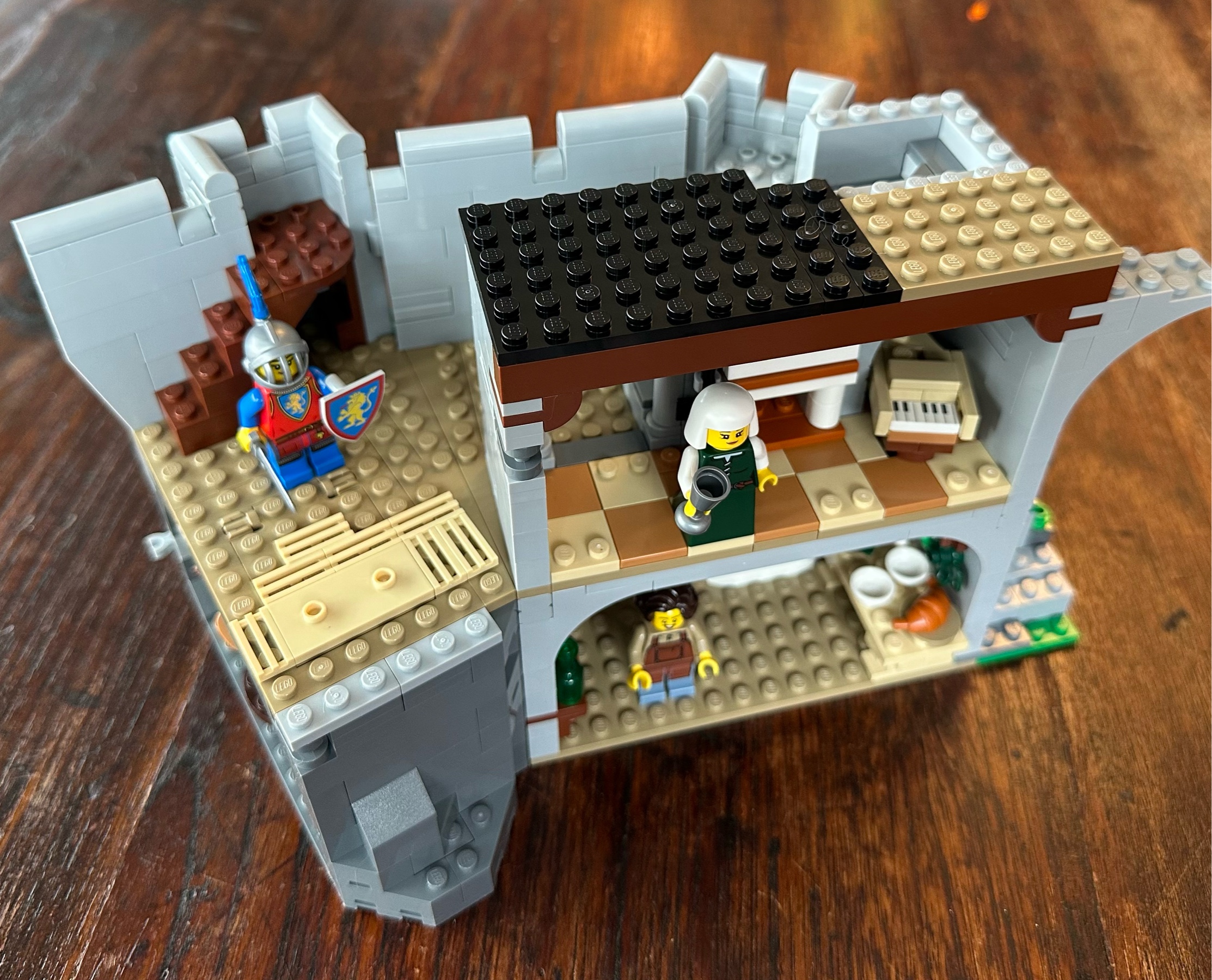 Interior view of castle with a fully roofed in music room in which there is a lady with her head covered in a white cloth. Is she a nun? Nearby stands a woman knight carrying a sword and shield. Her shield and tabard both display a lion sigil.