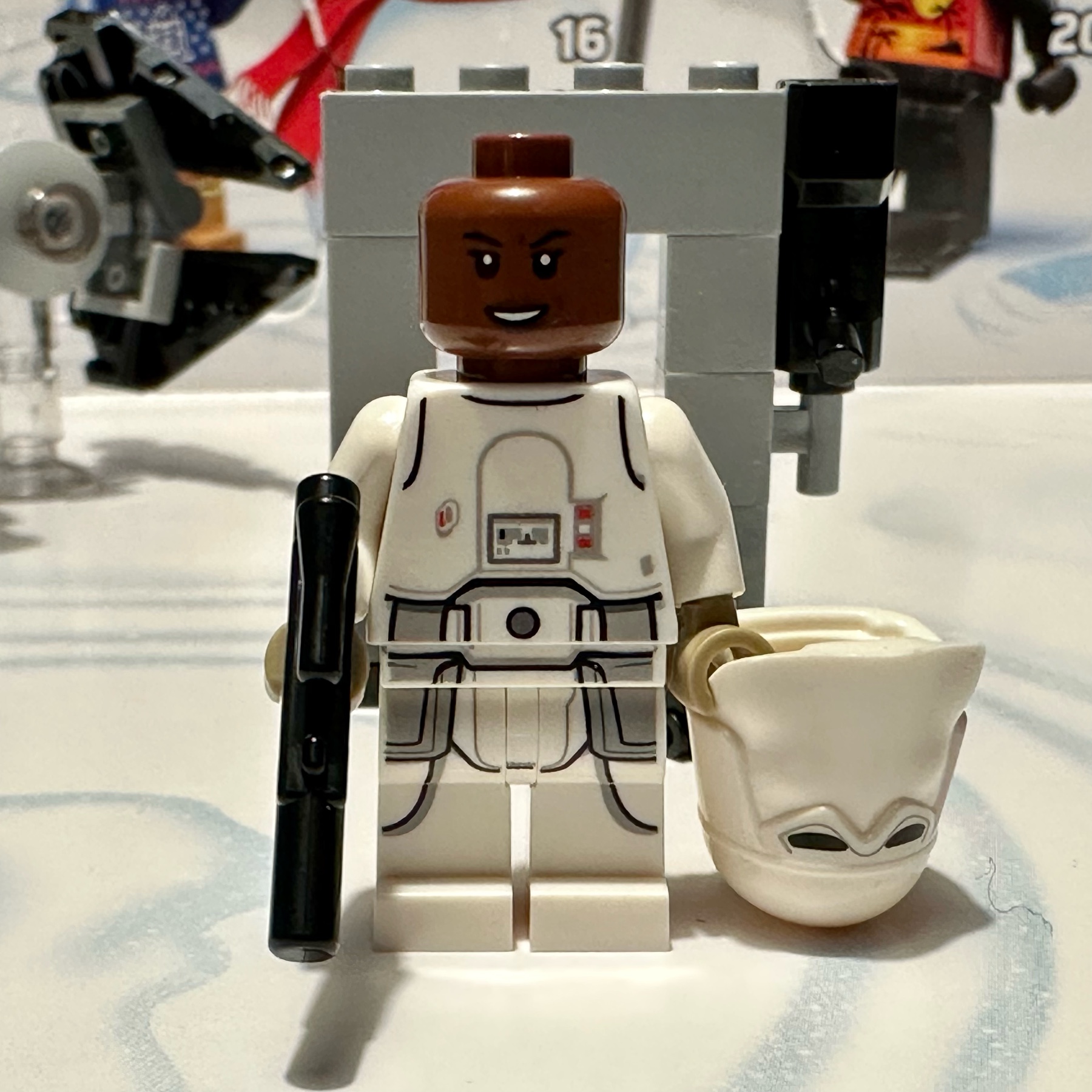 LEGO minifigure of a black woman in snowtrooper uniform holding a blaster in one hand and her helmet in the other