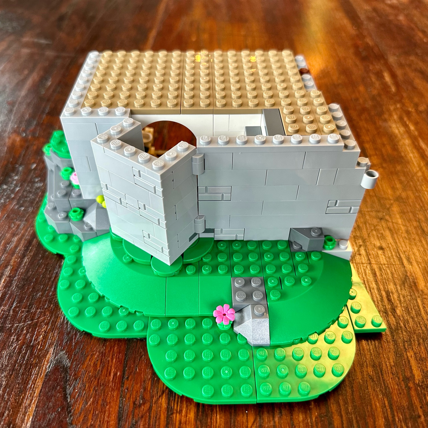 Exterior view of LEGO castle wall with some greenery. Part of the wall is pushed out at a 45° angle to the rest of the wall, perhaps to form a tower.