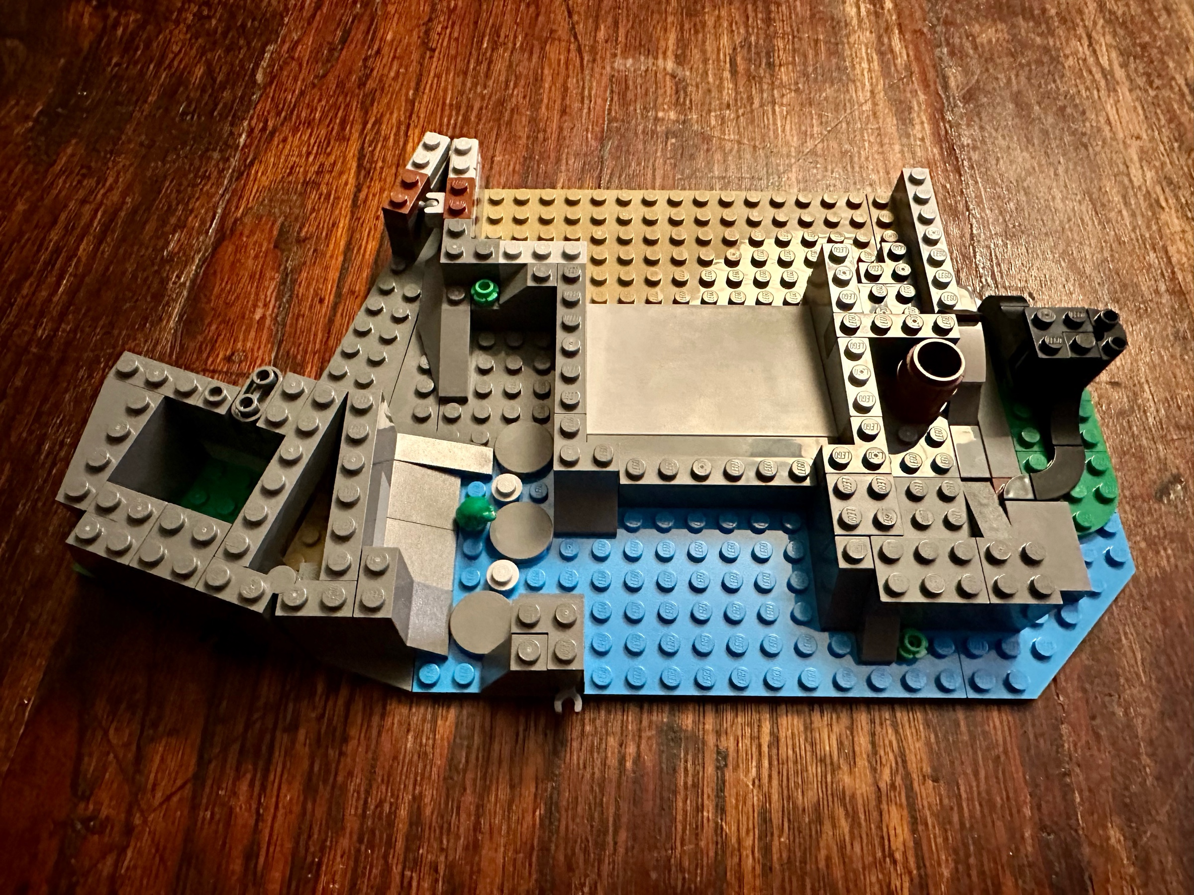 Foundations of LEGO castle showing water, stone, and an earthern floor. The roots of a black-trunked tree are on the right.