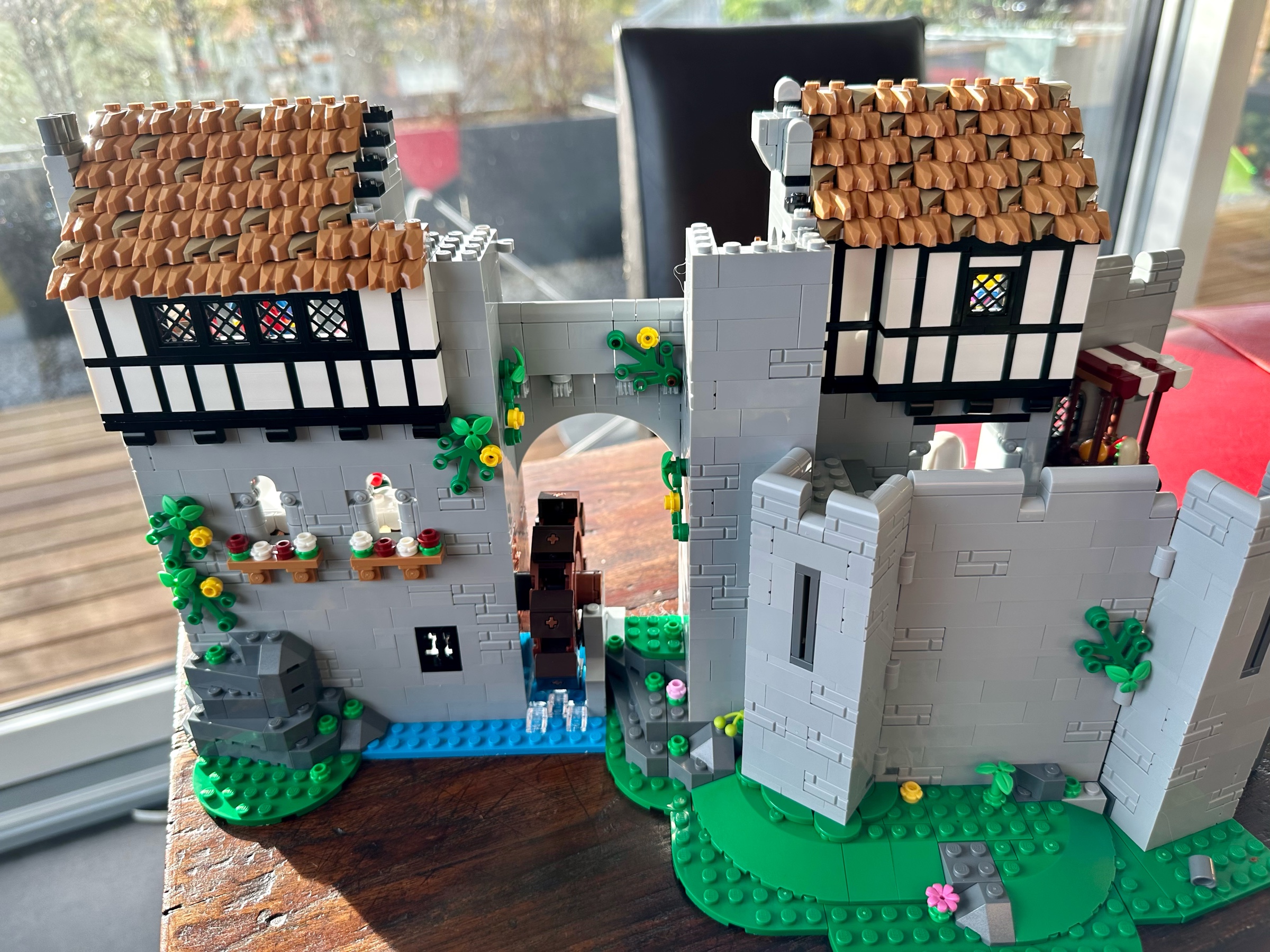 Exterior view of LEGO castle expanded. The lower floors are built of gray stone covered in some vines. The upper floor is built of white plaster and black wood and roofed with thatched straw.