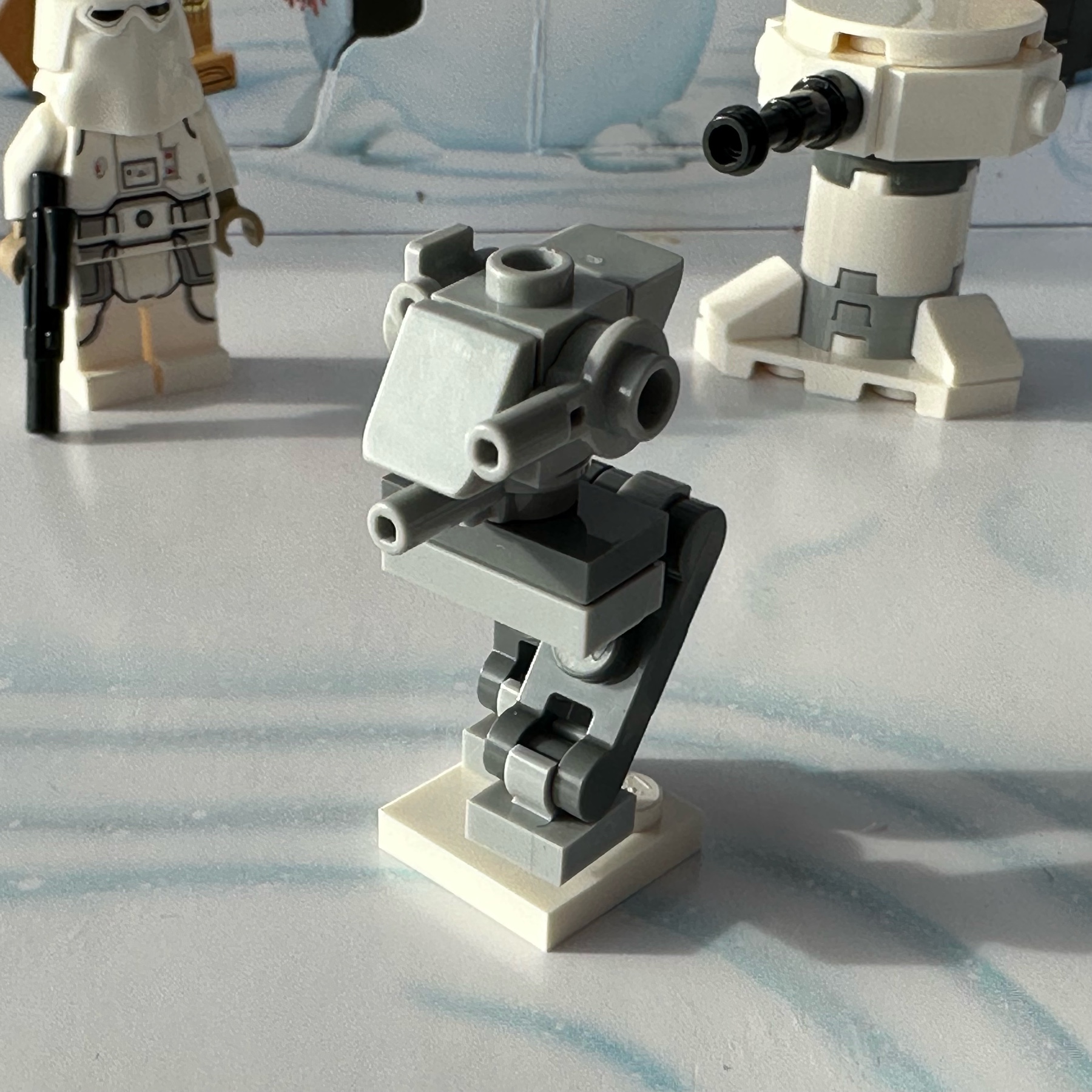LEGO micro-build mostly in light gray of an Imperial AT-ST, All-Terrain Scout Transport, a two-legged mechanical walker with guns. The 2022 version has a single central cannon and a side-mounted cannon.