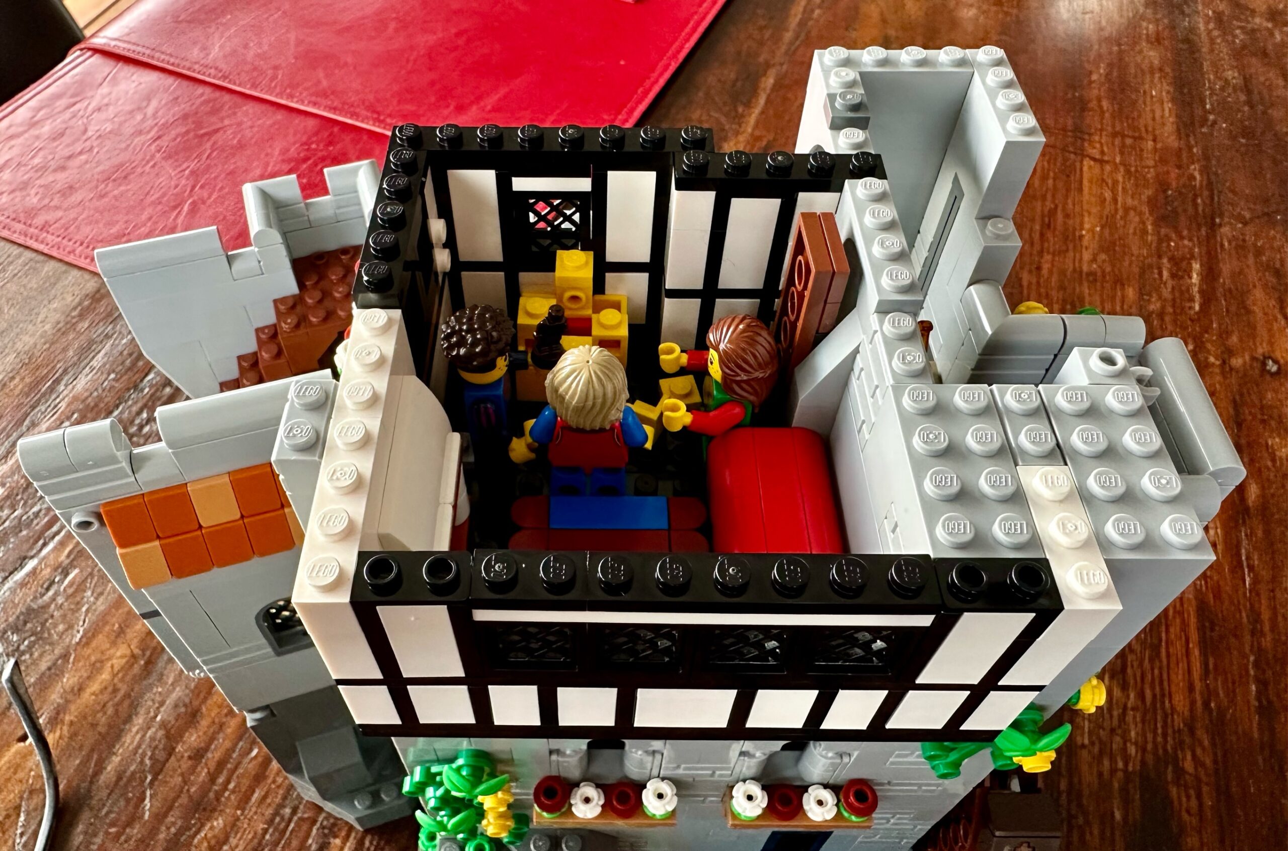 Top down view of LEGO castle in closed position to form a complete child's bedroom or playroom. Two young children play with toys while the frightened squire stands over them.