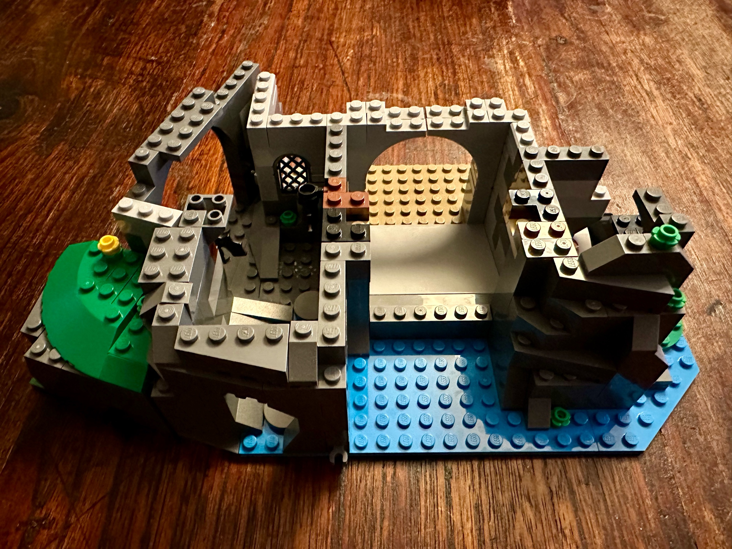 LEGO castle foundation with water in the front, a cave on the left and a room with some weapons on the right.
