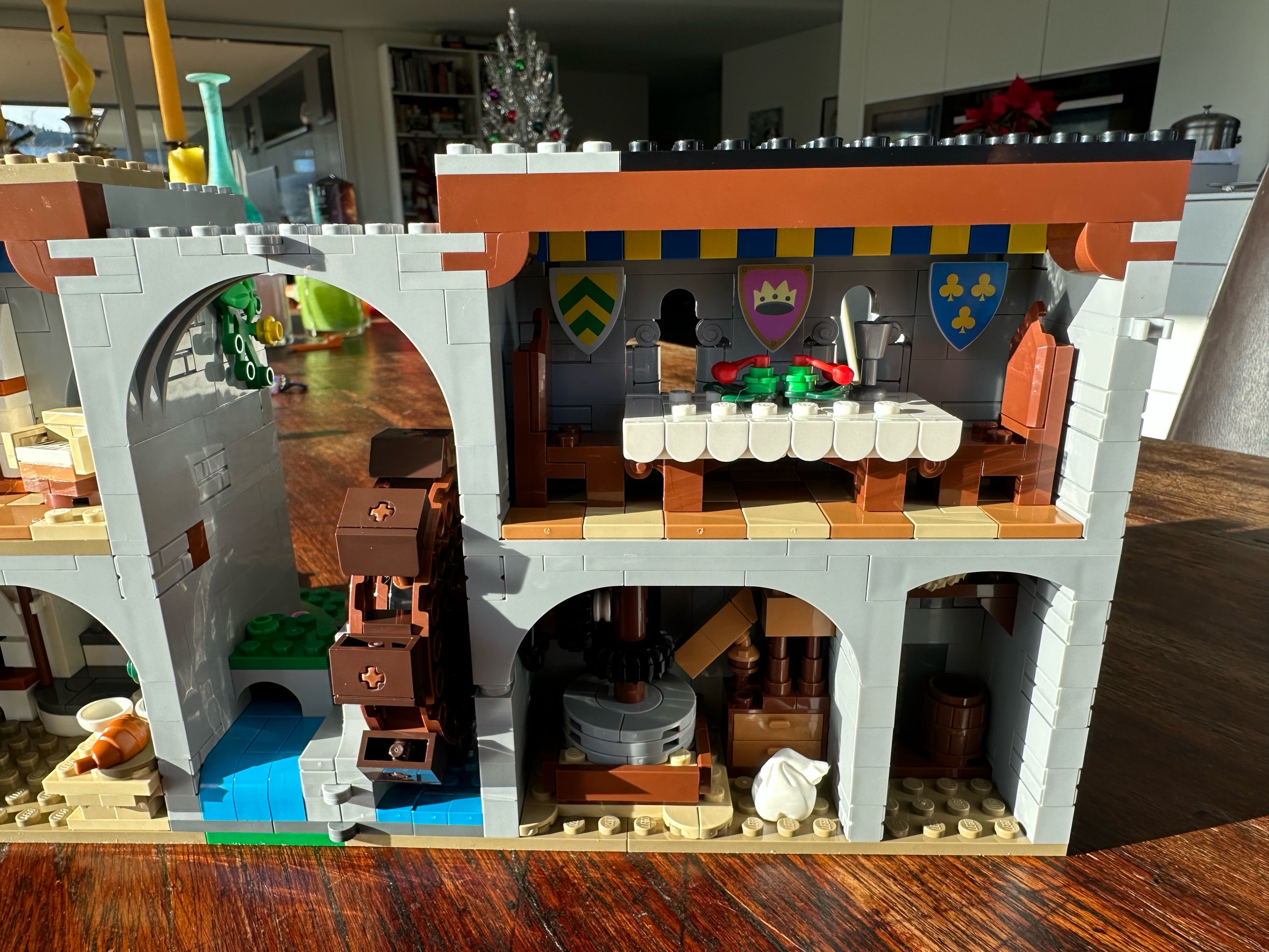 Interior view of LEGO castle section showing a banquet table, two chairs, three shields hung on the wall, and a blue and yellow banner.