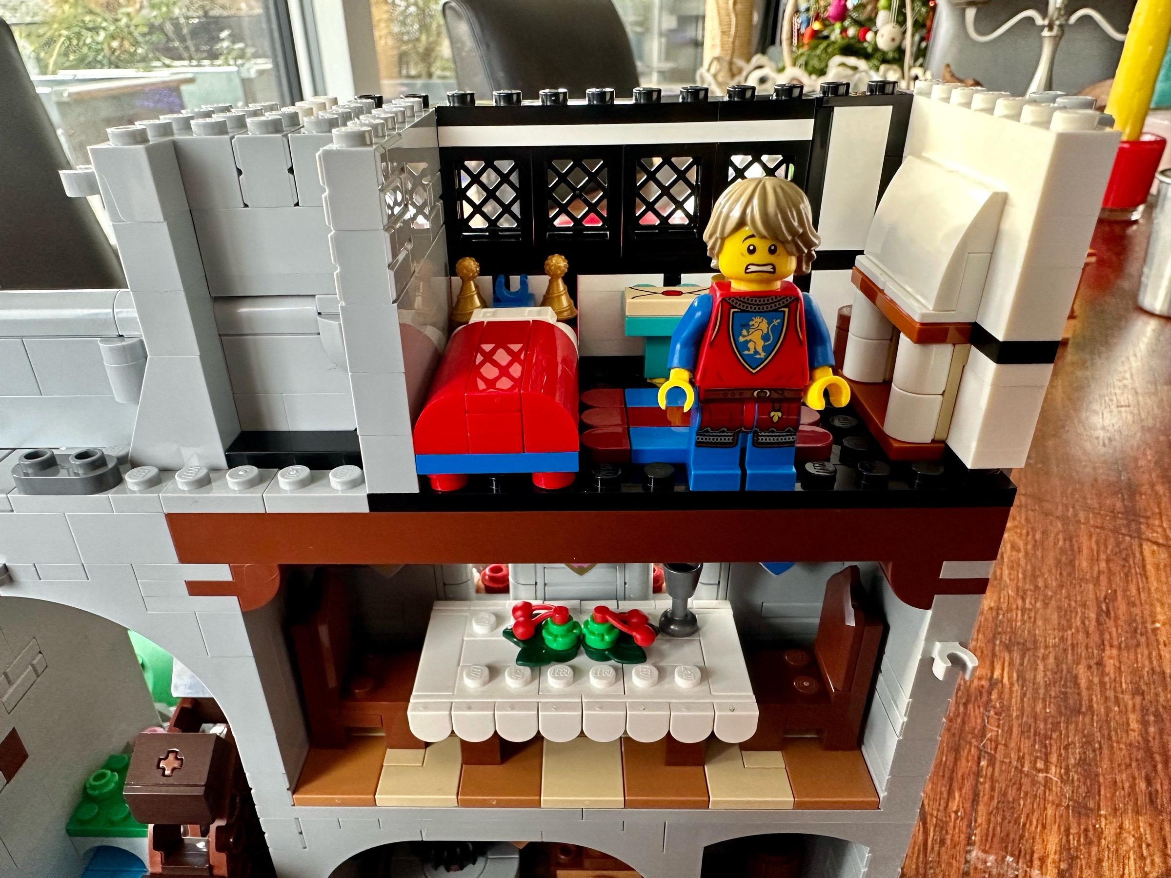 Interior view of LEGO castle child's room with bed on left, desk in the middle, and fireplace on the right. A young squire with a frightened expression stands in front of the desk.