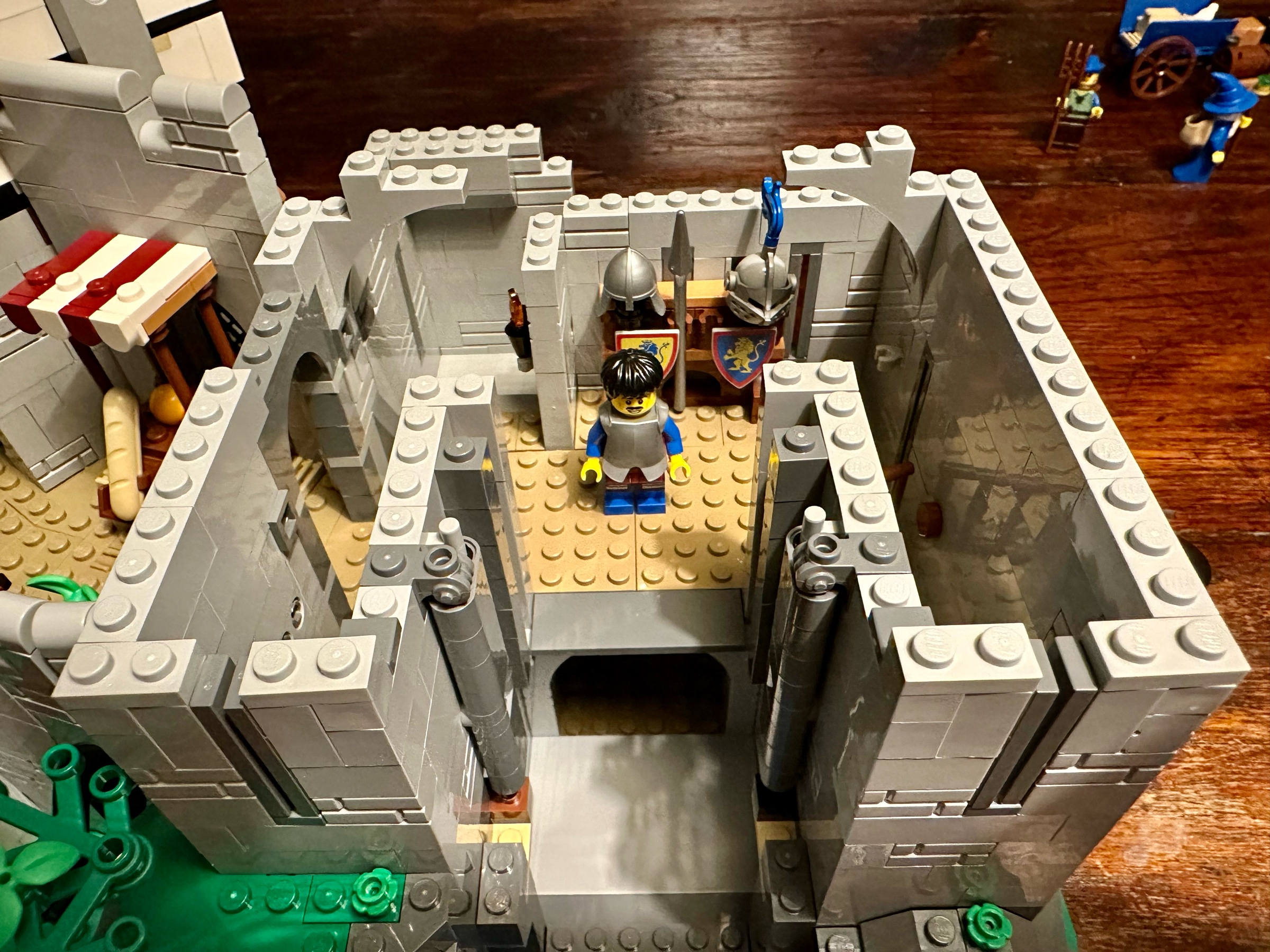LEGO castle armory with an armored knight and a stand holding two shields, two helmets, and a spear.