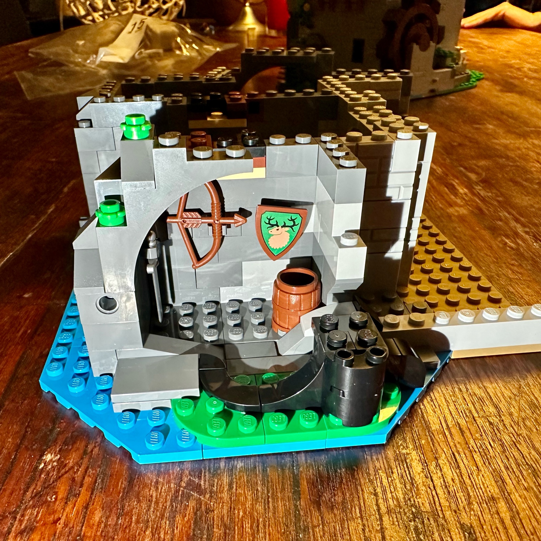 LEGO secret room with sword, bow, and shield hanging on the wall and a barrel standing on the floor.