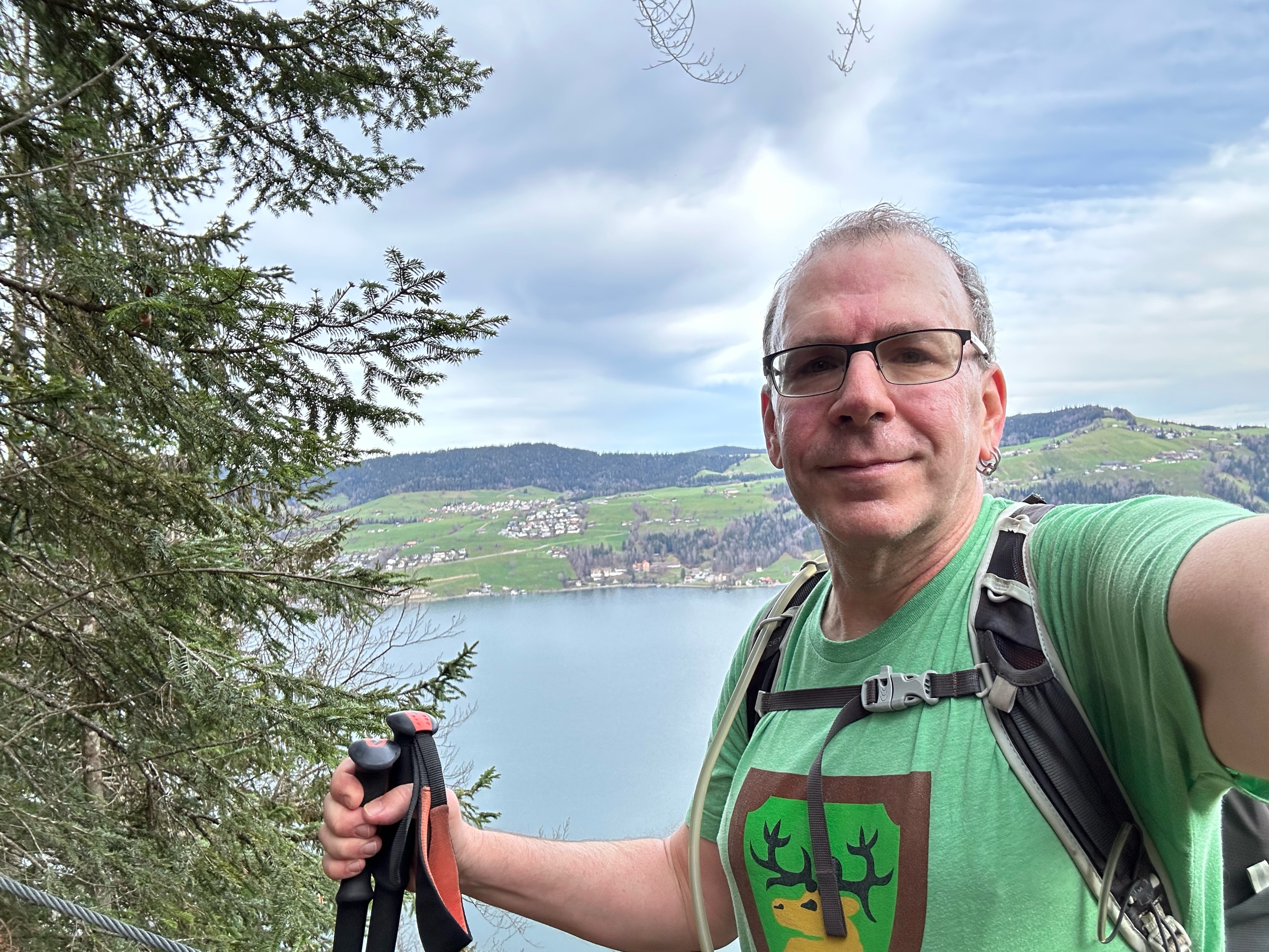 Selfie of a man with a backpack and hiking poles in front of a lake.