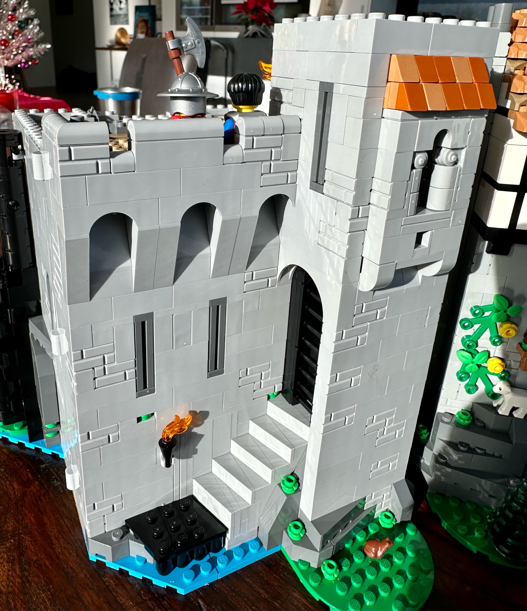 Exterior view of LEGO castle showing a black portcullis lowered at the top of a flight of stairs. Above the backs of two guards can be seen leaning against the parapet.