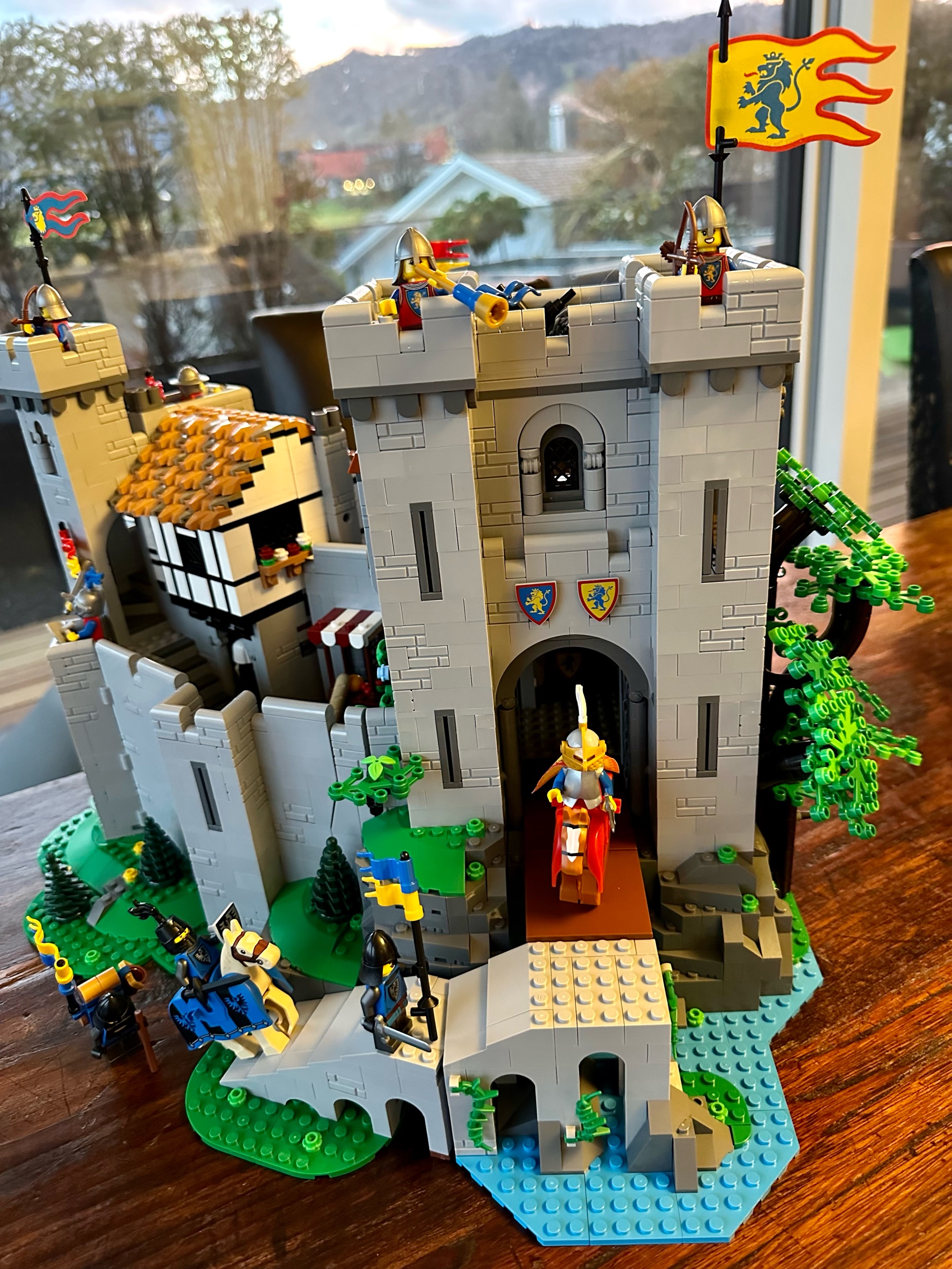 LEGO castle with a lowered drawbridge and a stone ramp. Three knights approach the ramp while the queen sits atop her horse at the top to greet them.