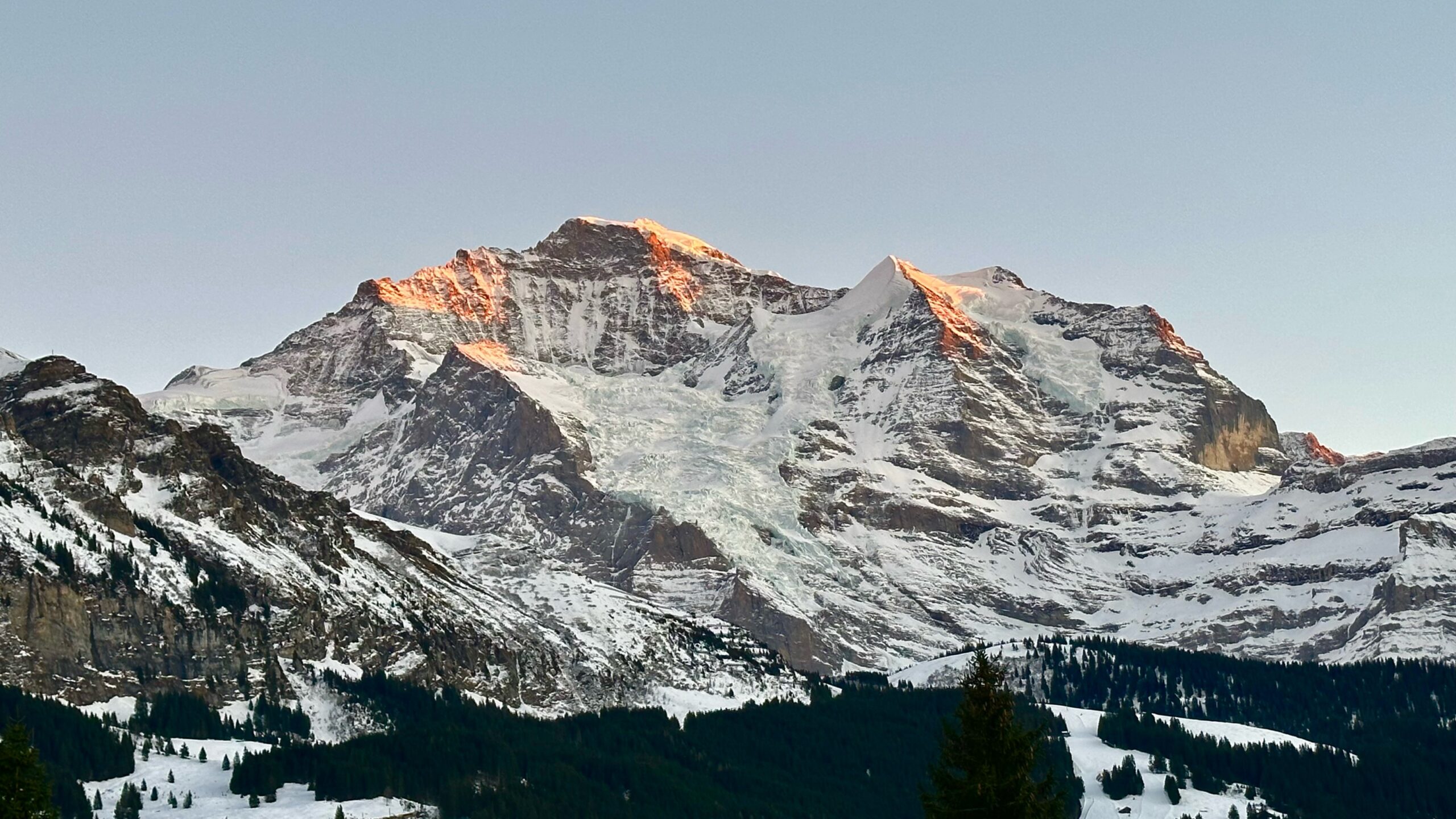 The Jungfrau, a rocky and snow peak in the Swiss Alps, with a few small peaks reflecting the rosy light of sunset.