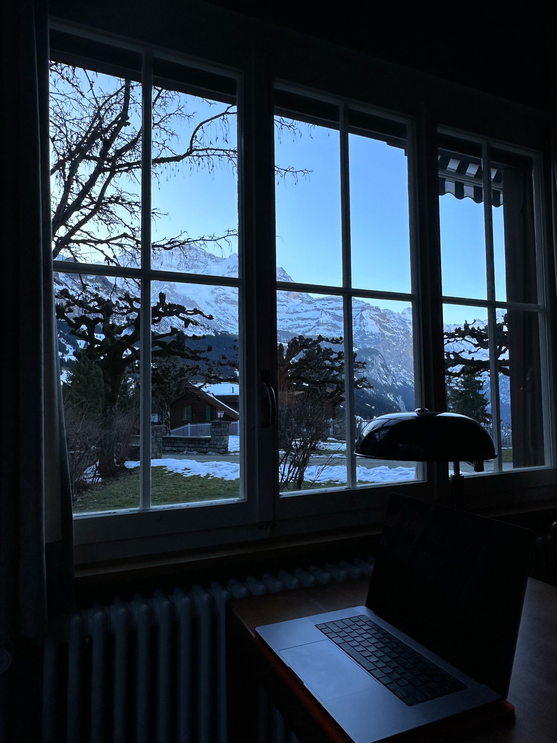 Laptop on a small table in front of a window with a view of snow-covered mountains in the Swiss Alps.