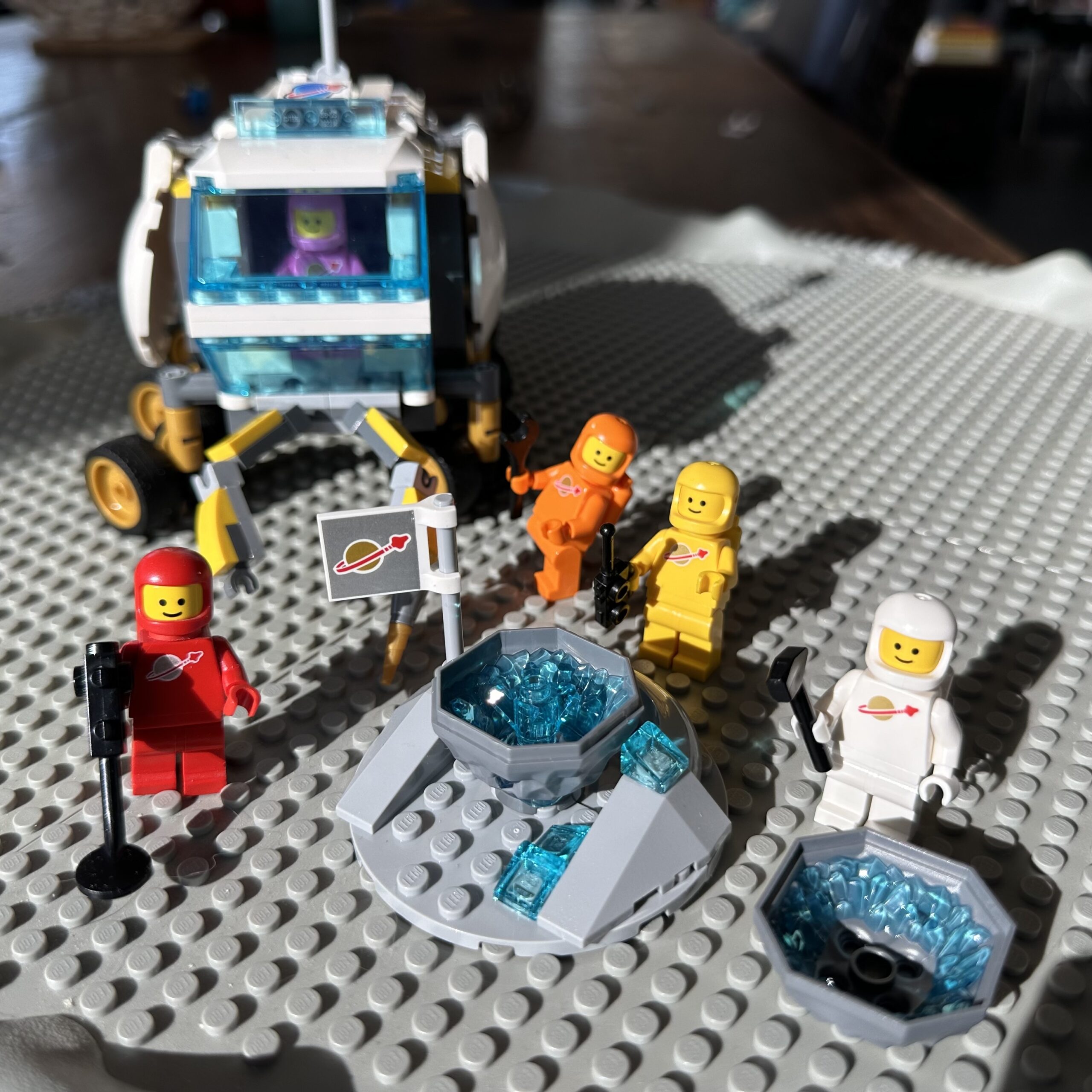 Modern LEGO moon rover set on old-school gray crater plate and populated with multiple colorful classic space guys.