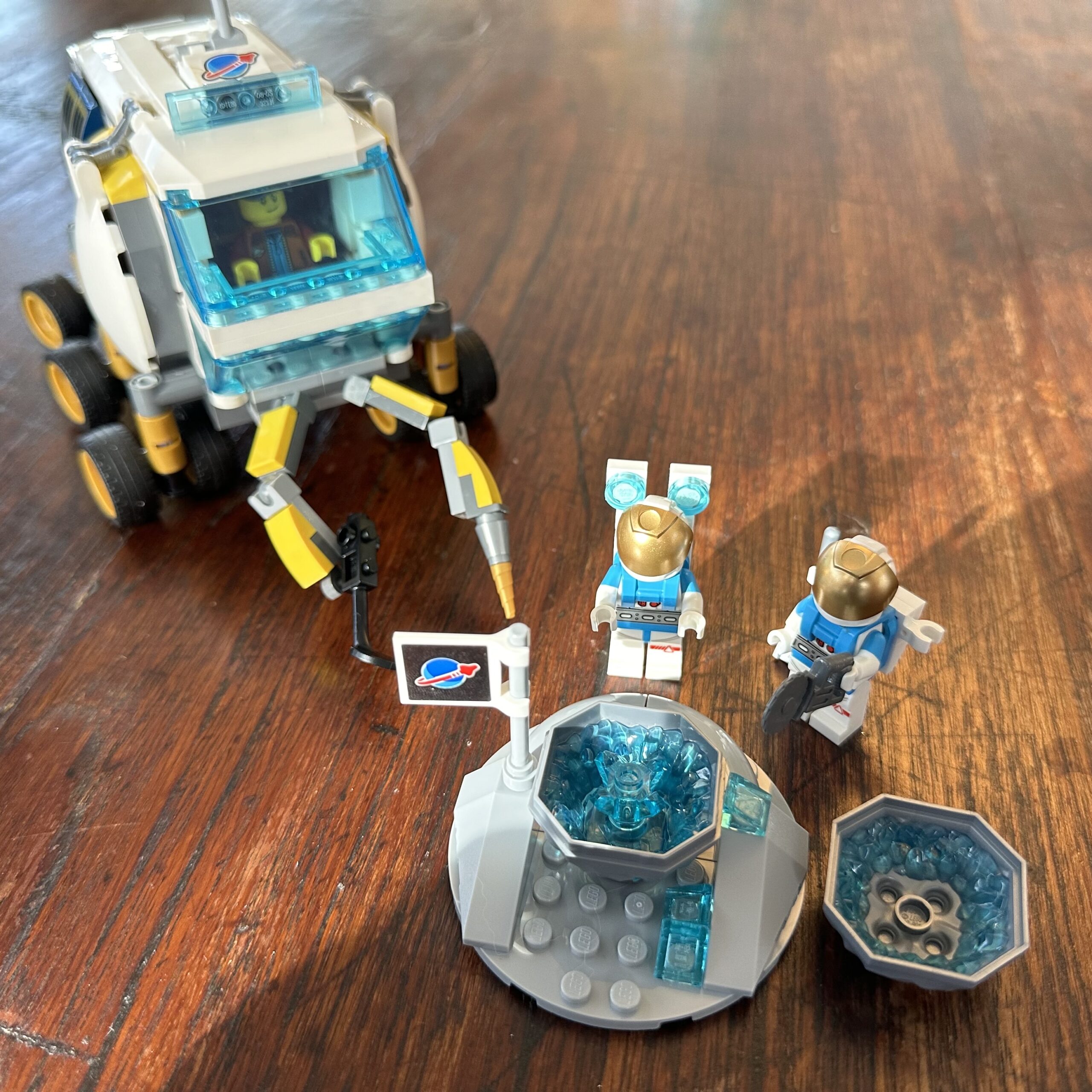 Two LEGO astronauts open a geode with crystal inside. A driver sits in a lunar rover nearby.