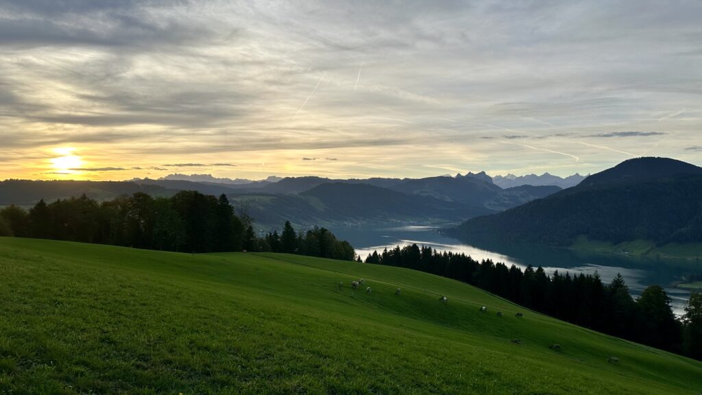 View of lake and distant mountains with the sun just over the horizon on a cloudy morning.