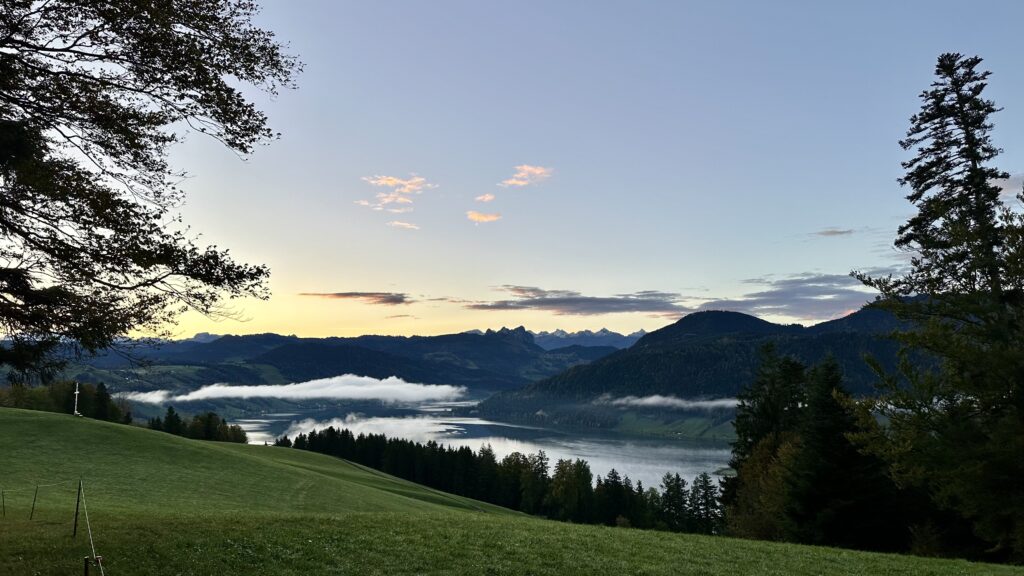 View of a lake surrounded by hills and mountains at sunrise.