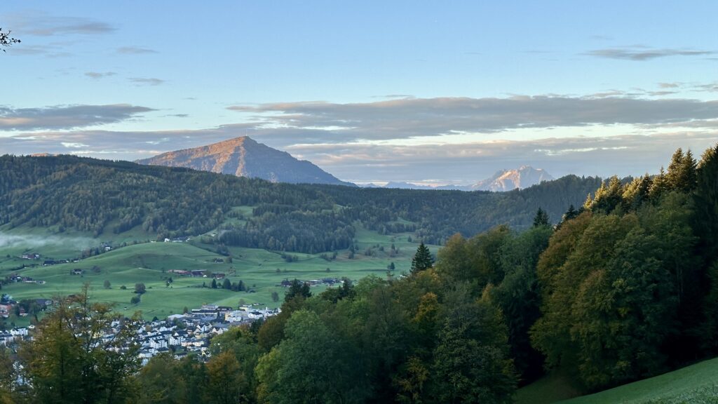 View across a green valley with two mountains in the distance, both illuminated by early morning light.