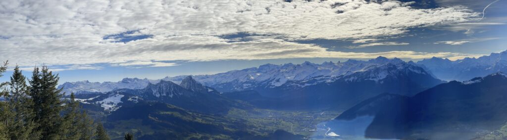 Panorama view of snow-covered mountains in the distance past a green valley underneath a mostly cloudy sky. Photo taken from the Wildspitz, the highest mountain in canton Zug. What does this have to do with paid software? Nothing. I just like mountains. And walking up them (walking back down again, less so).