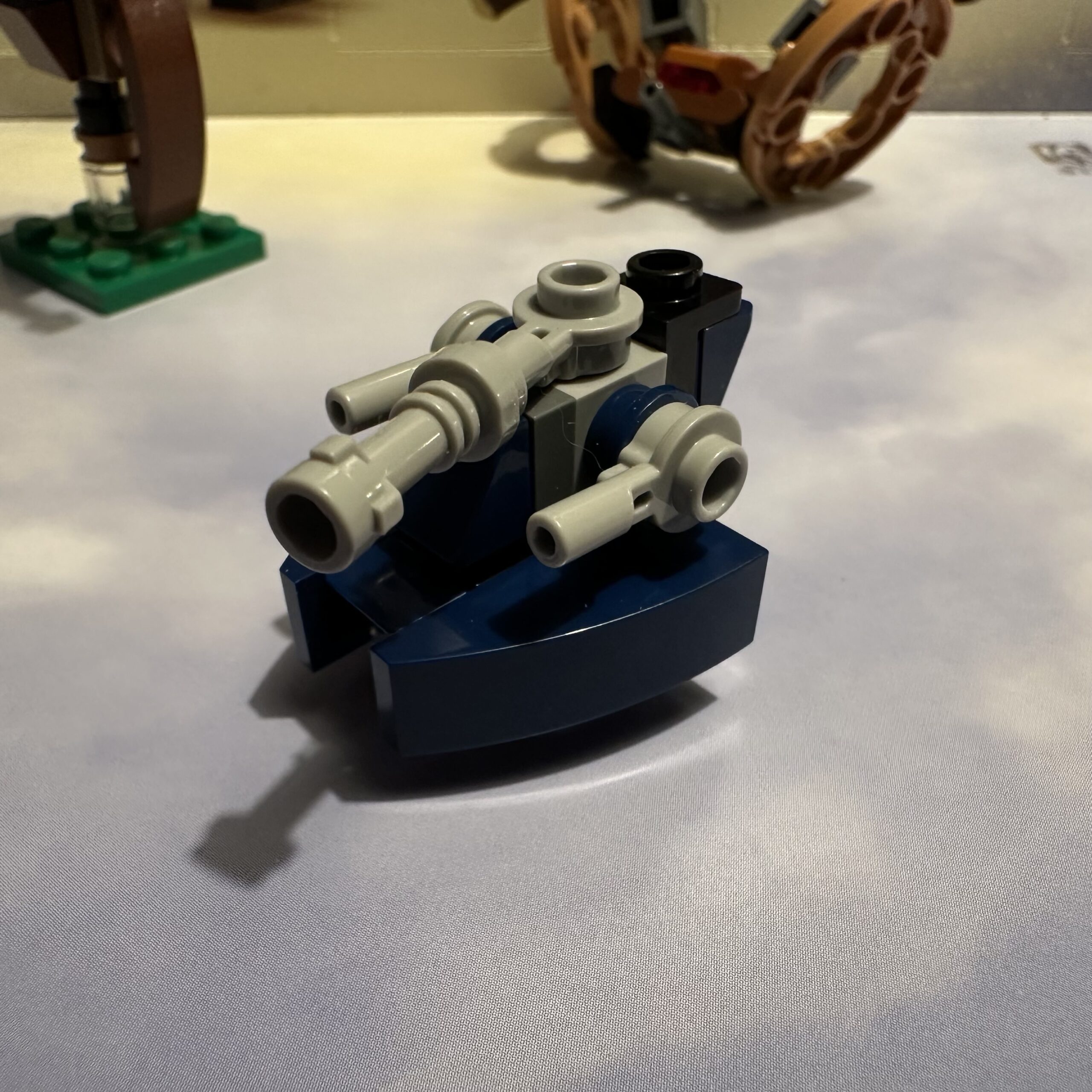 LEGO micro-build of a tank with a dark blue lower body and light gray upper. There are two small side cannons and one large central cannon.
