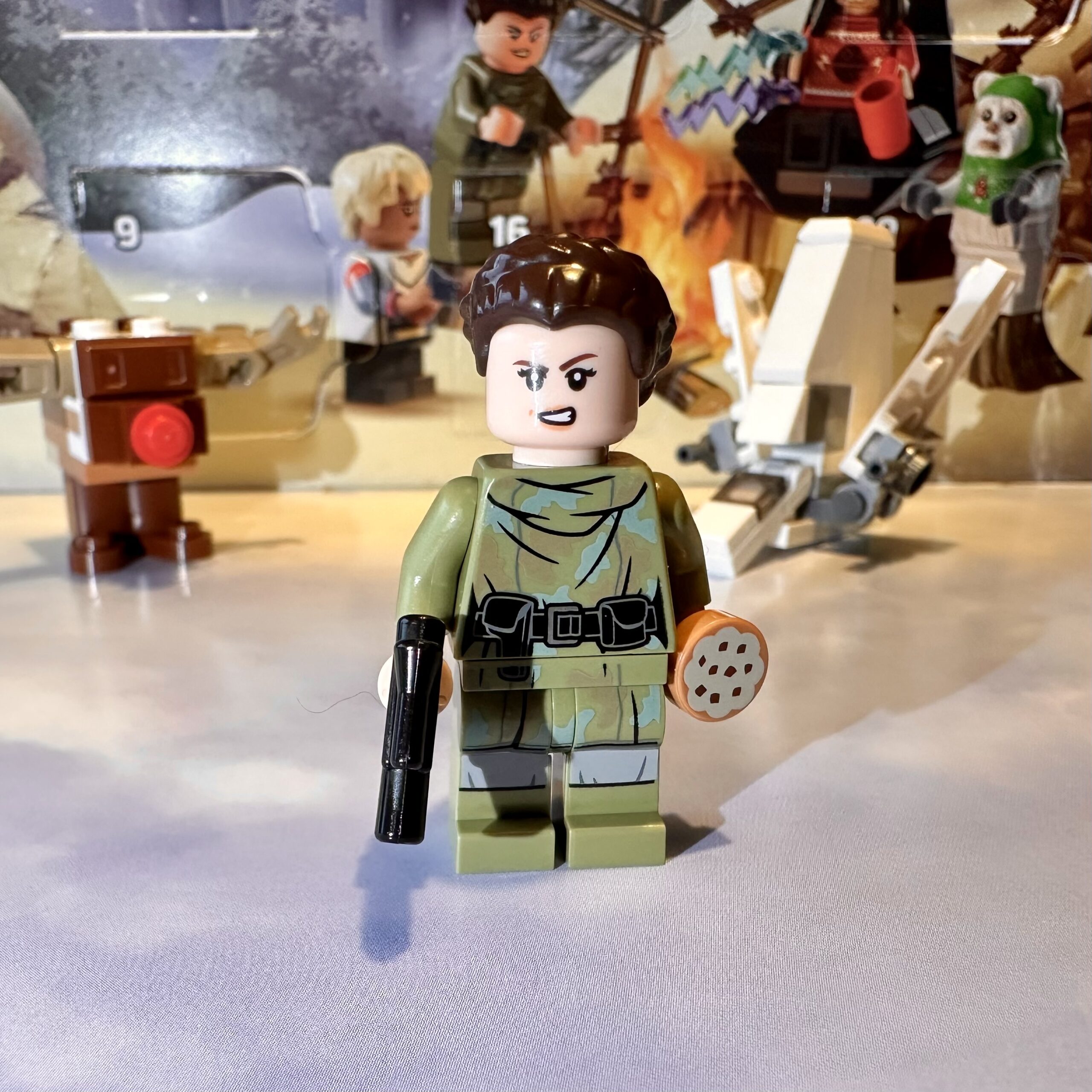 LEGO minifigure of Return of the Jedi era Princess Leia in her Endor moon forest camouflage outfit. She holds a small blaster in her right hand and a cookie in her left.