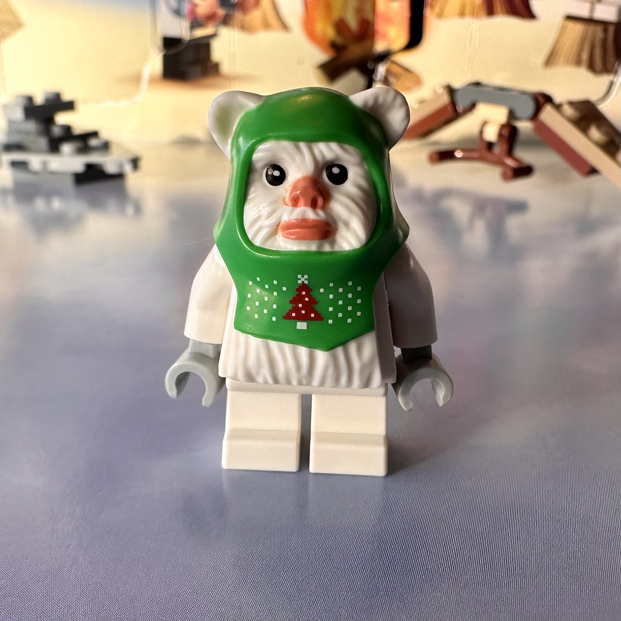 LEGO ewok minifigure. The ewok is white and it's wearing a green headdress with an ugly-sweater style Christmas tree and snow pattern on it.