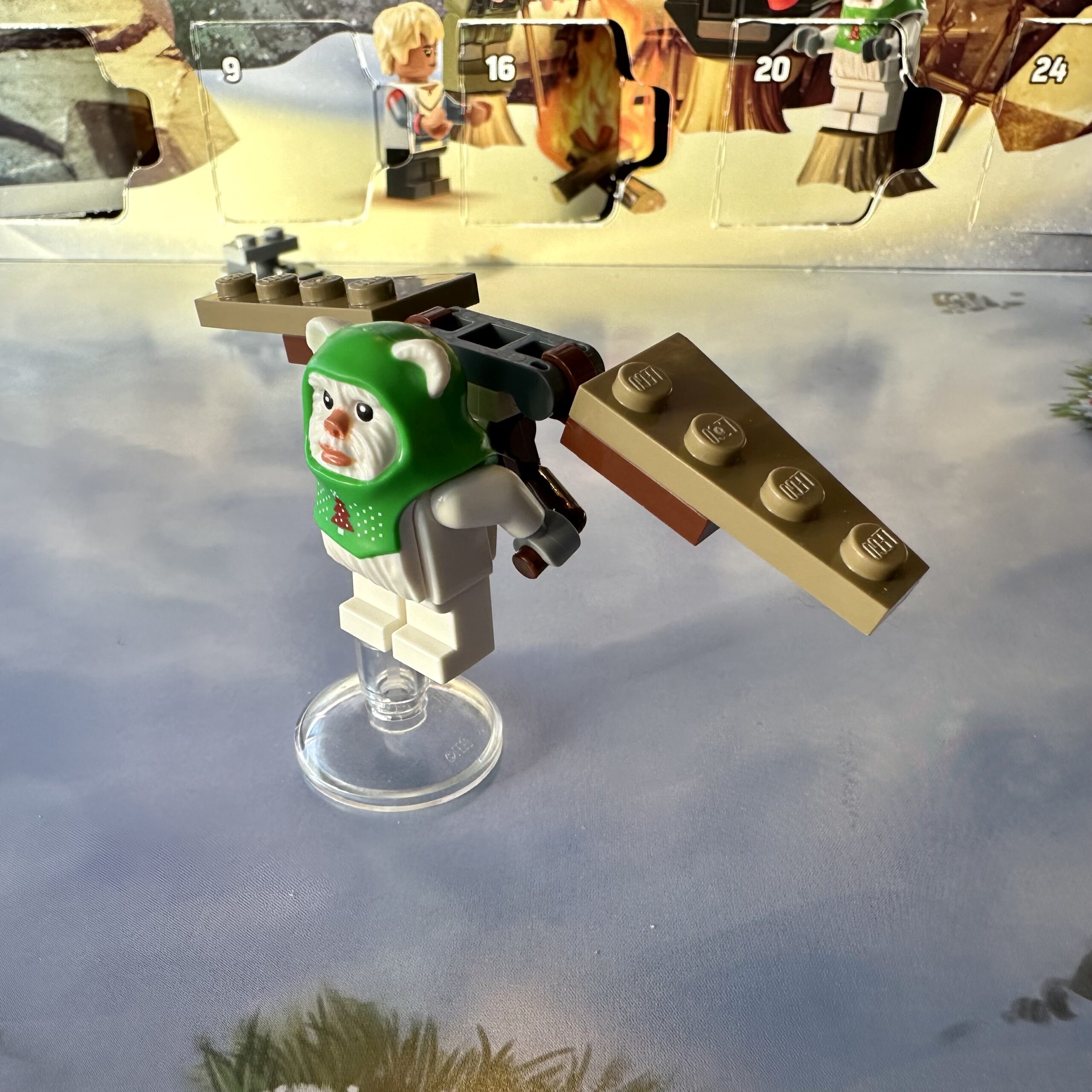 White LEGO ewok minifigure wearing a green ugly sweater Christmas headdress holding onto a primitive hang glider.