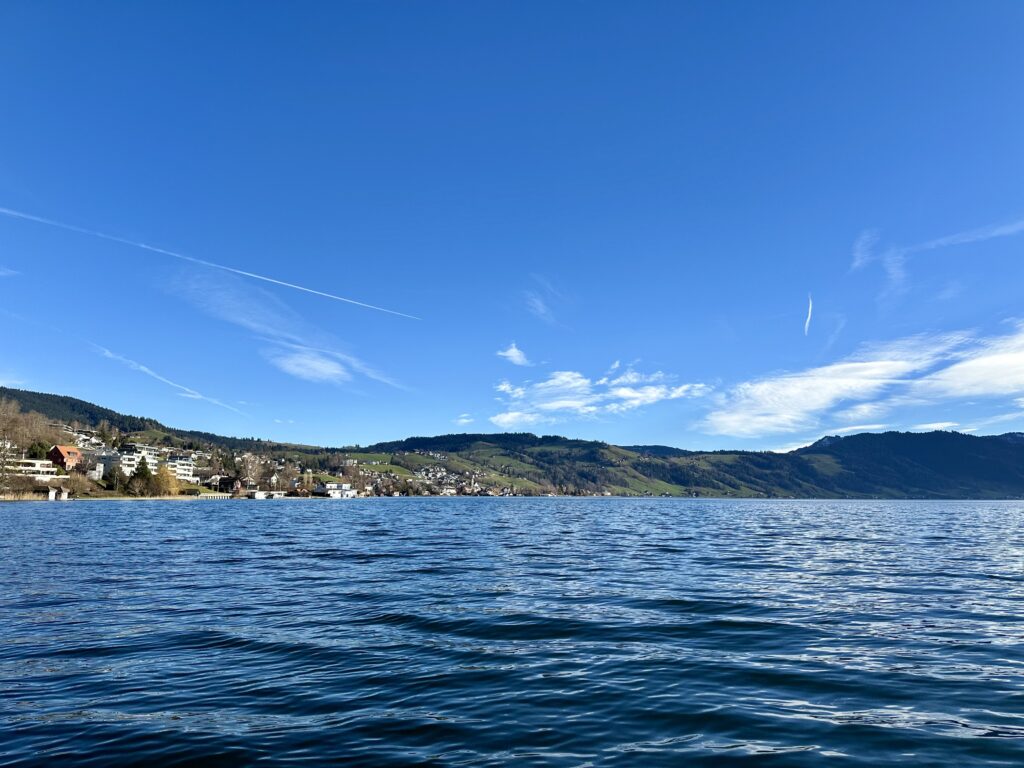 Lake view on a sunny winter’s day. Hills with some buildings edge the lake. The water looks dark blue and is ever so slightly choppy.