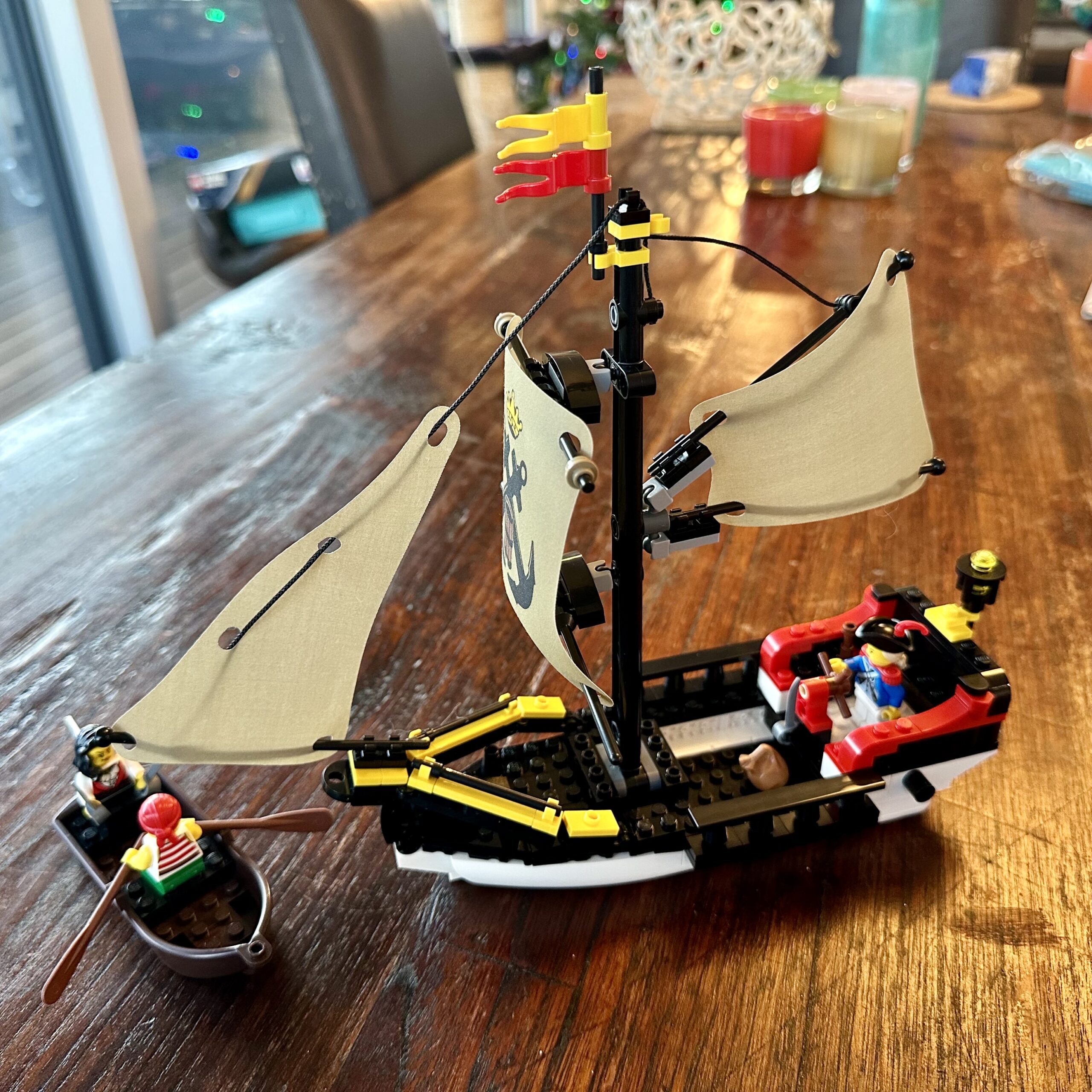 LEGO sailing ship with one mast and three sails piloted by a single soldier. A brown rowboat crewed by two pirates, one rowing and the other holding a pair of cutlasses.