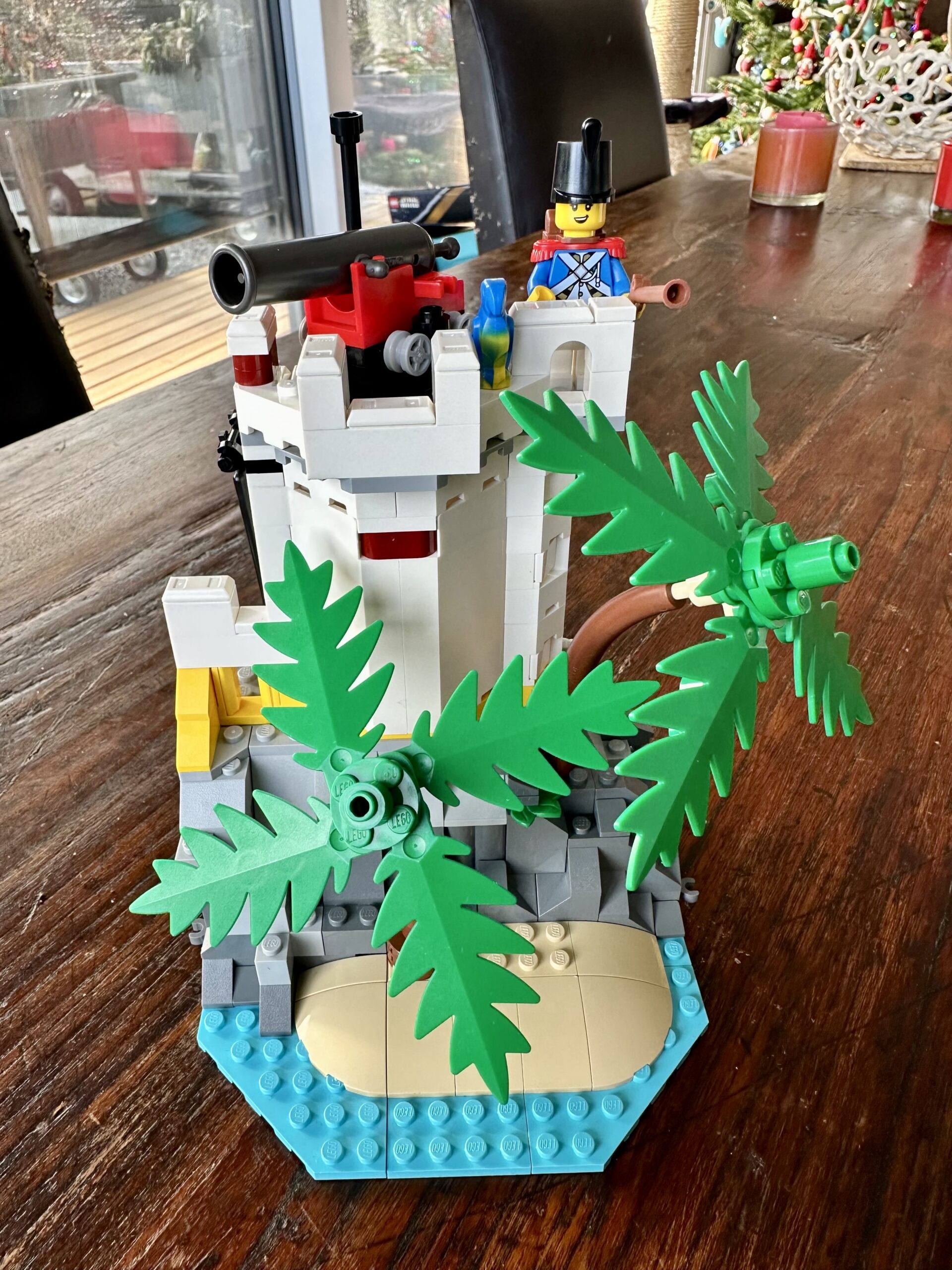 LEGO build of set 10320 Eldorado Fortress in progress. A small white tower with cannon and an Imperial Guard atop it. A sand beach and two palm trees are in front.