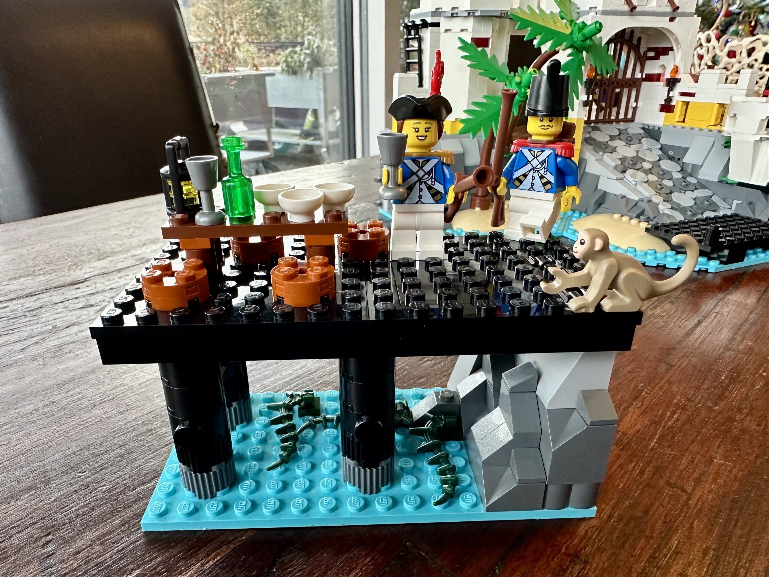 LEGO build of set 10320 Eldorado Fortress in progress. A small black jetty bearing a table set for a feast. Two Imperial guards look to be celebrating with a monkey.