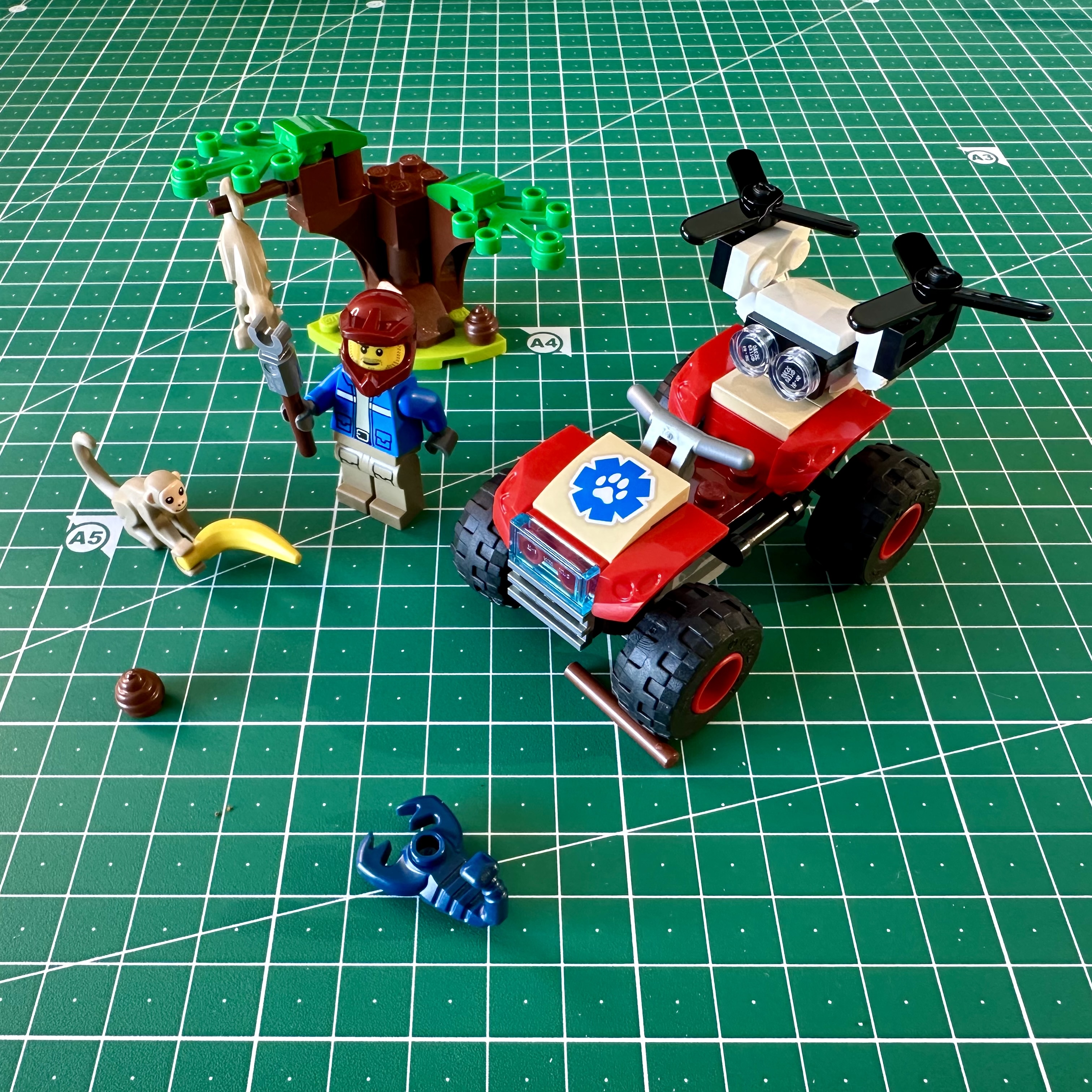LEGO ATV with a drone on the back, a minifigure in a helmet and holding a clawed pole for animal handling, a tree, two monkeys, and a scorpion.