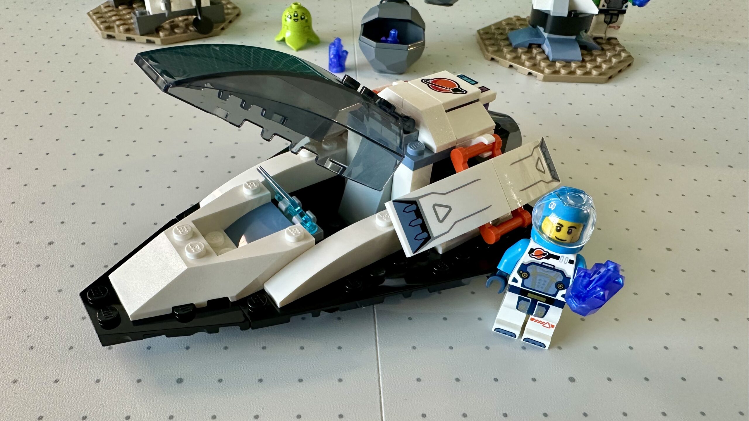 Close up of a chunky LEGO spaceship in black and white with a shaded cockpit canopy that is currently raised. An astronaut in an azure and white suit holds a purple crystal.