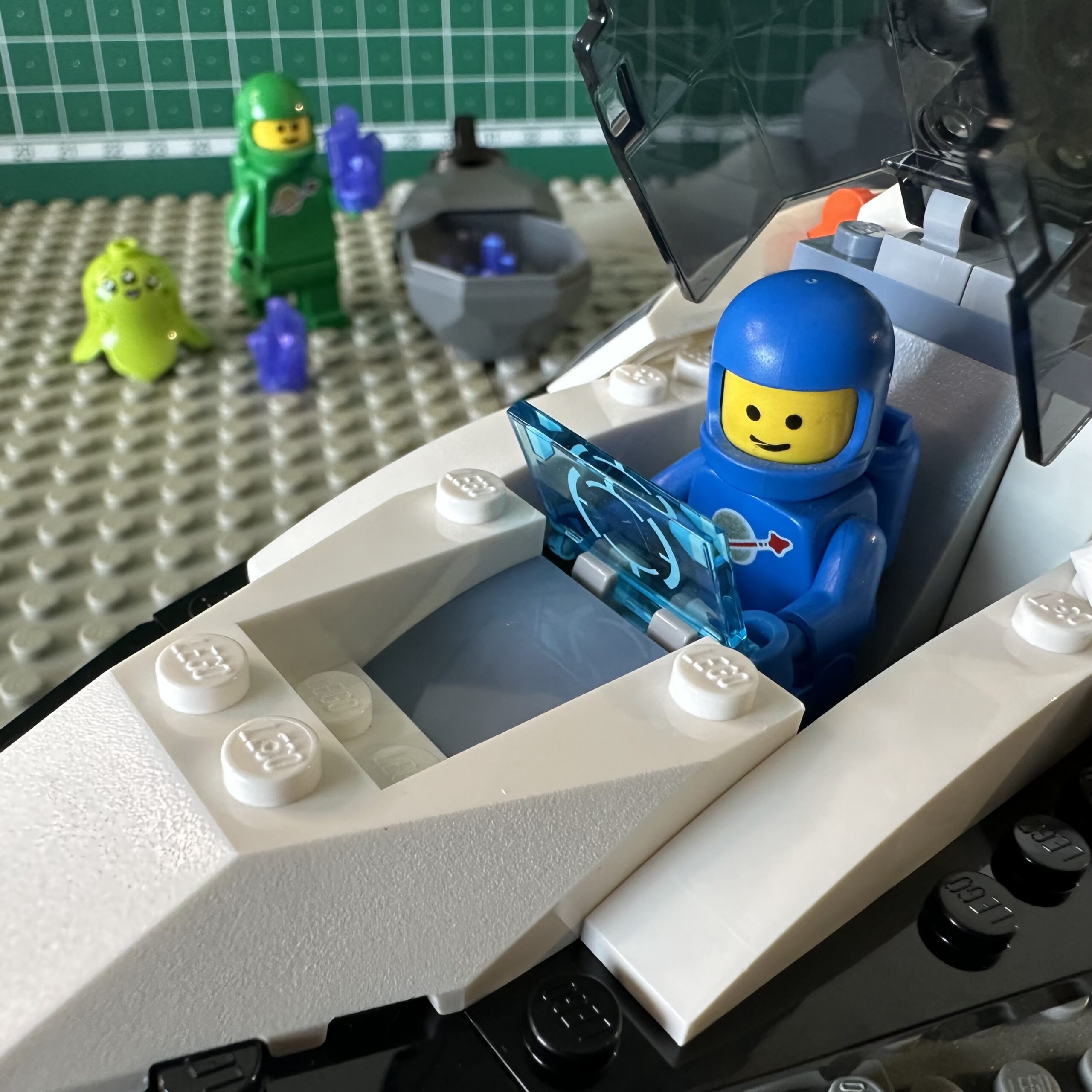 Spaceship from the 2024 Spaceship and Asteroid Recovery set piloted by a blue Classic Space astronaut. In the background a green Classic Space astronaut lifts a purple crystal from an asteroid. 