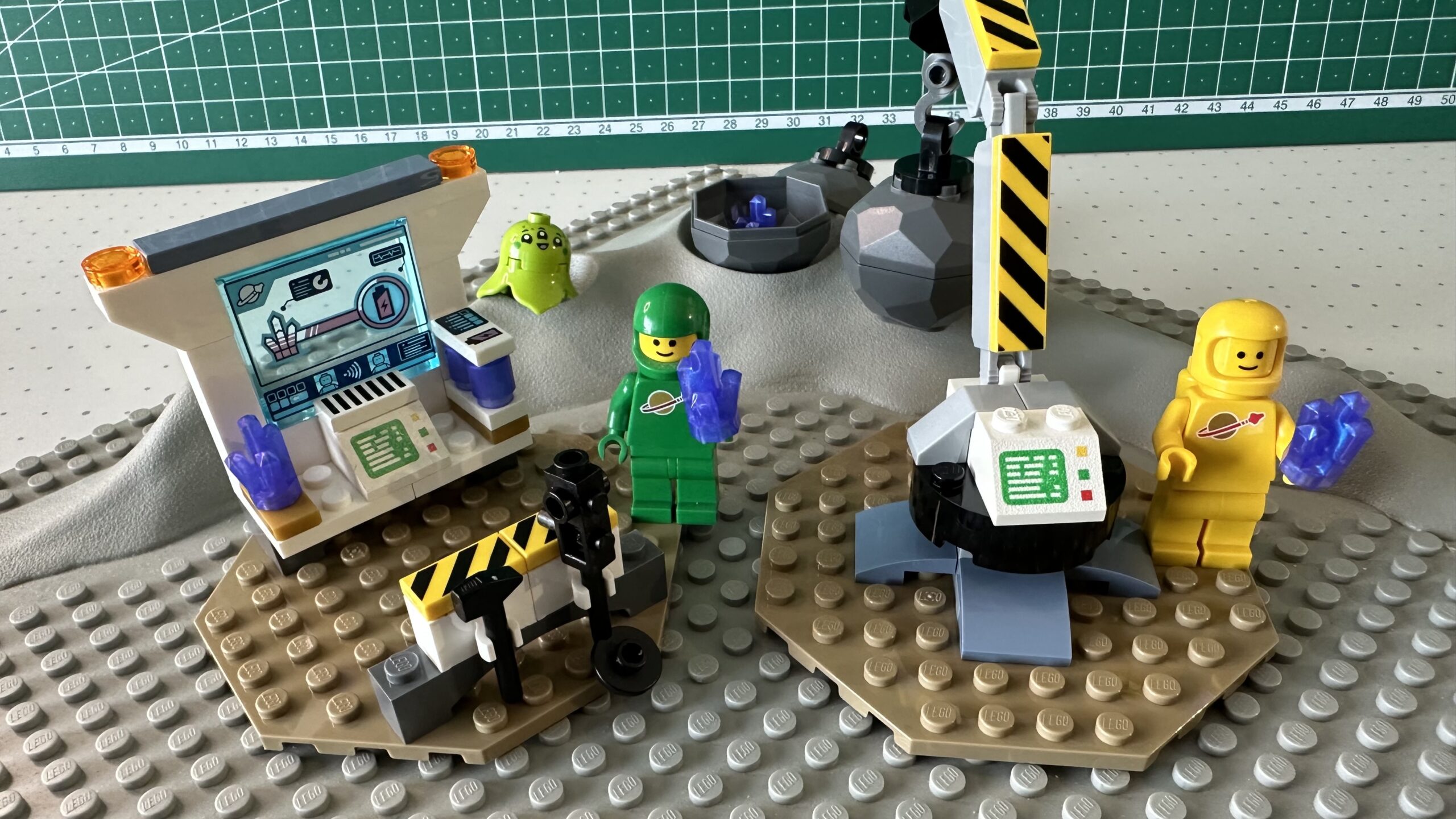Science station and crane from the 2024 Spaceship and Asteroid Recovery set operated by green and yellow Classic Space astronauts. Posed on a classic gray crater baseplate from the 1970's. The printed computer slopes and tools have been replaced with versions from the 1970's and 1980's, and printed yellow and black hazard stripe tiles have been added to the crane and tool rack.