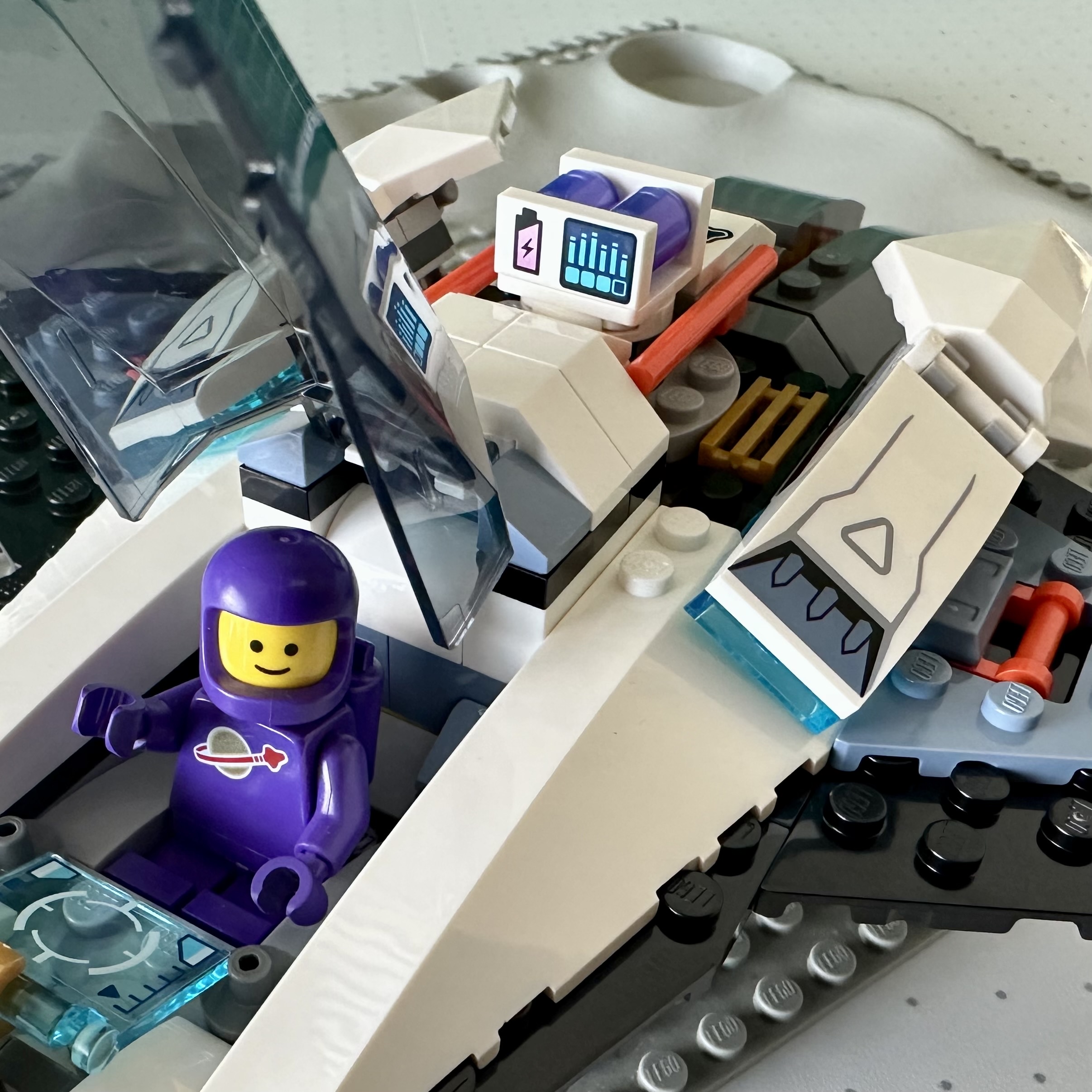 Spaceship from the 2024 Interstellar Spaceship LEGO set piloted by a purple Classic Space astronaut. Posed on a classic gray crater baseplate from the 1970's.