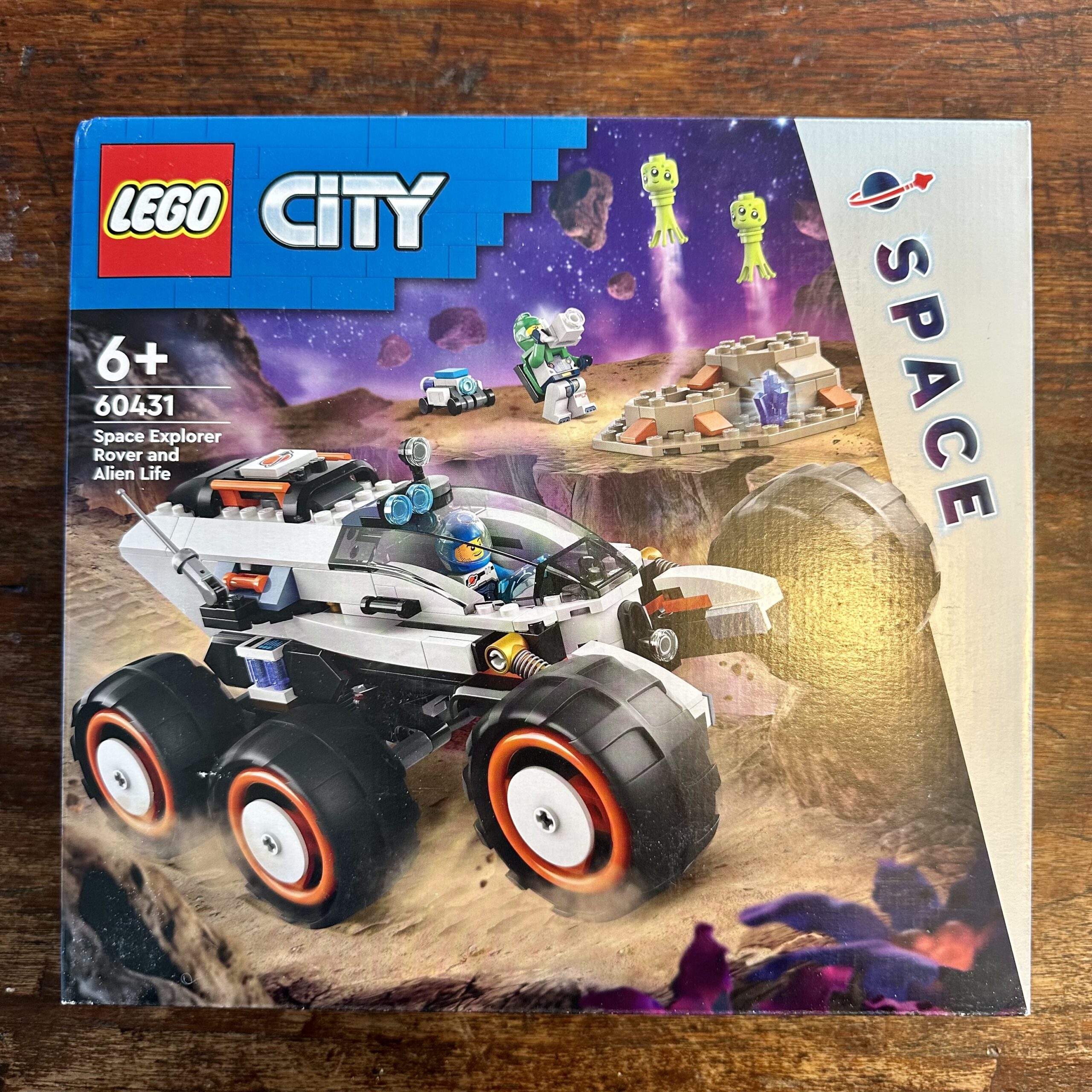Box for LEGO City Space set 60431 Space Explorer Rover and Alien Life. Box depicts a 6-wheeled rover in white and black with orangish-red highlights piloted by a blue astronaut across alien terrain. In the background a green astronaut photographs some green aliens launching from a pair of dark tan craters. A small wheeled robot sits nearby.