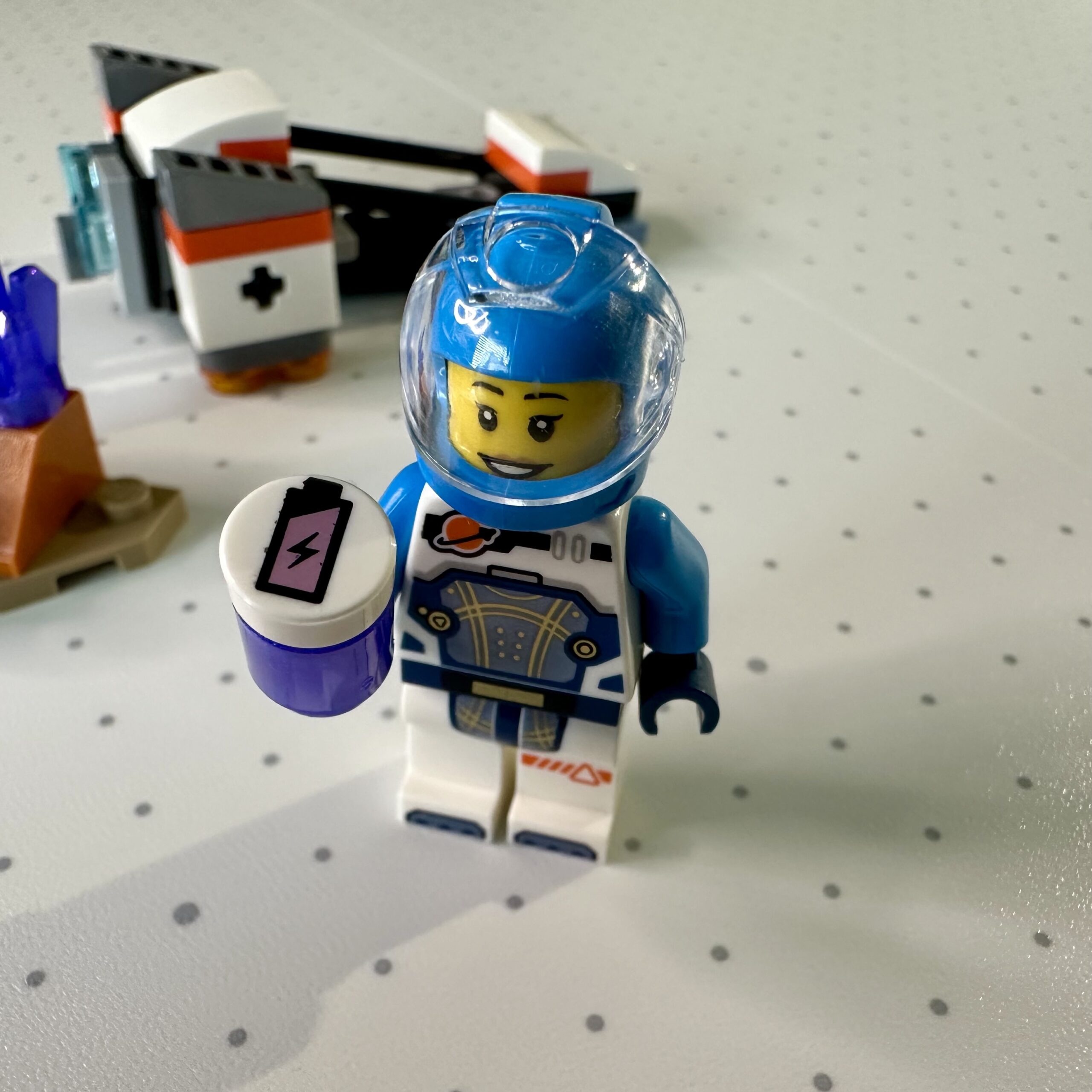 Closeup of white and azure-suited astronaut holding a purple battery canister showing a mostly full charge.
