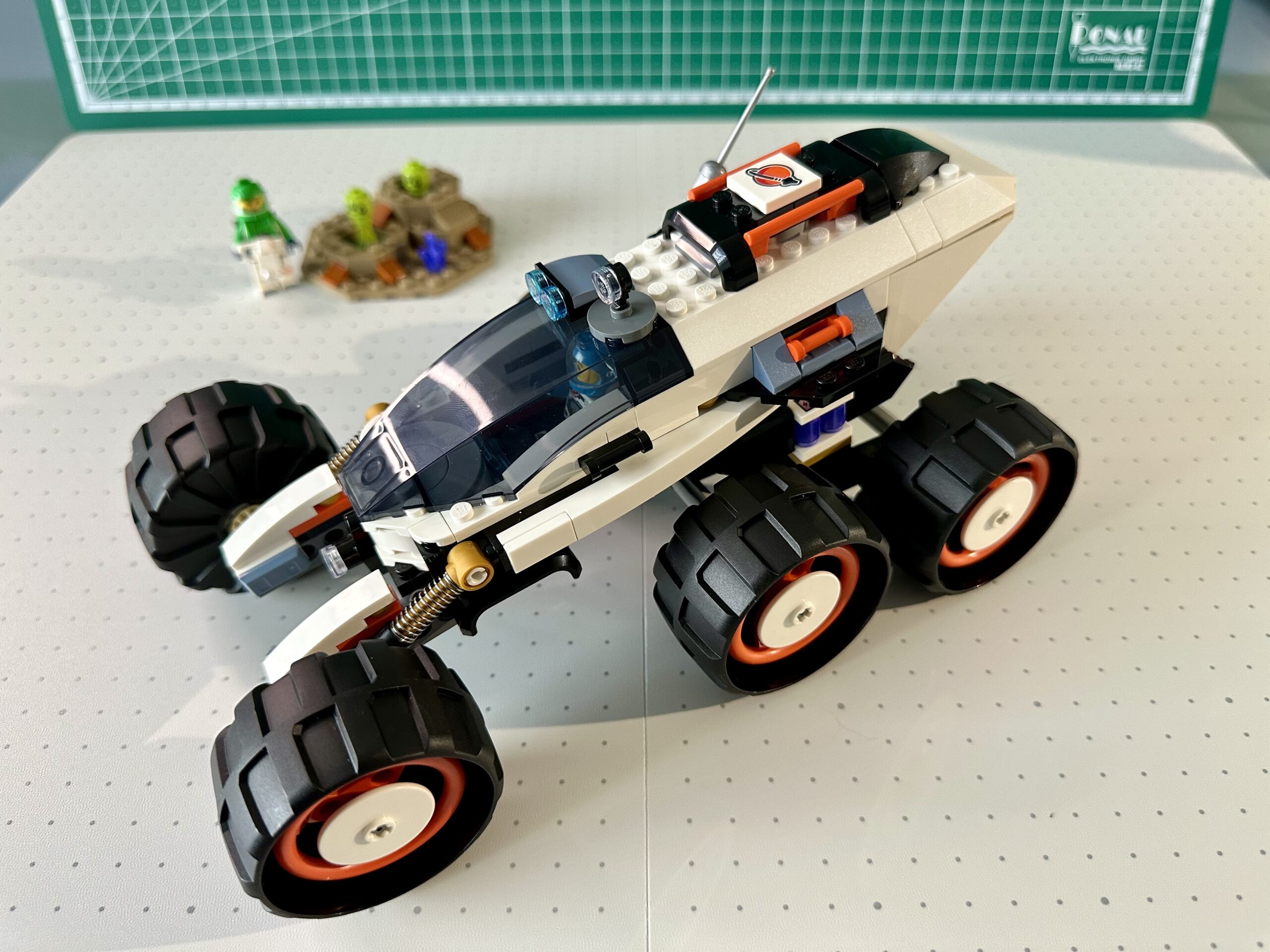 Six-wheeled rover in white with black and reddish orange trim. With its raised suspension it looks a bit like a monster truck.