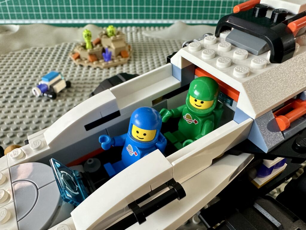 Blue and green LEGO Classic Space astronaut minifigures crew the rover from the 2024 set number 60431. Posed on a pair of classic gray crater baseplates from the 1970's.